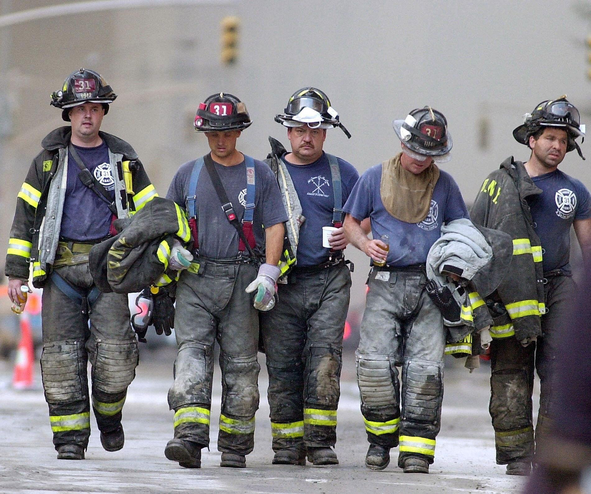 Six firefighters walking together, wearing firefighting gear and helmets, on a paved surface with orange traffic cones in the background.