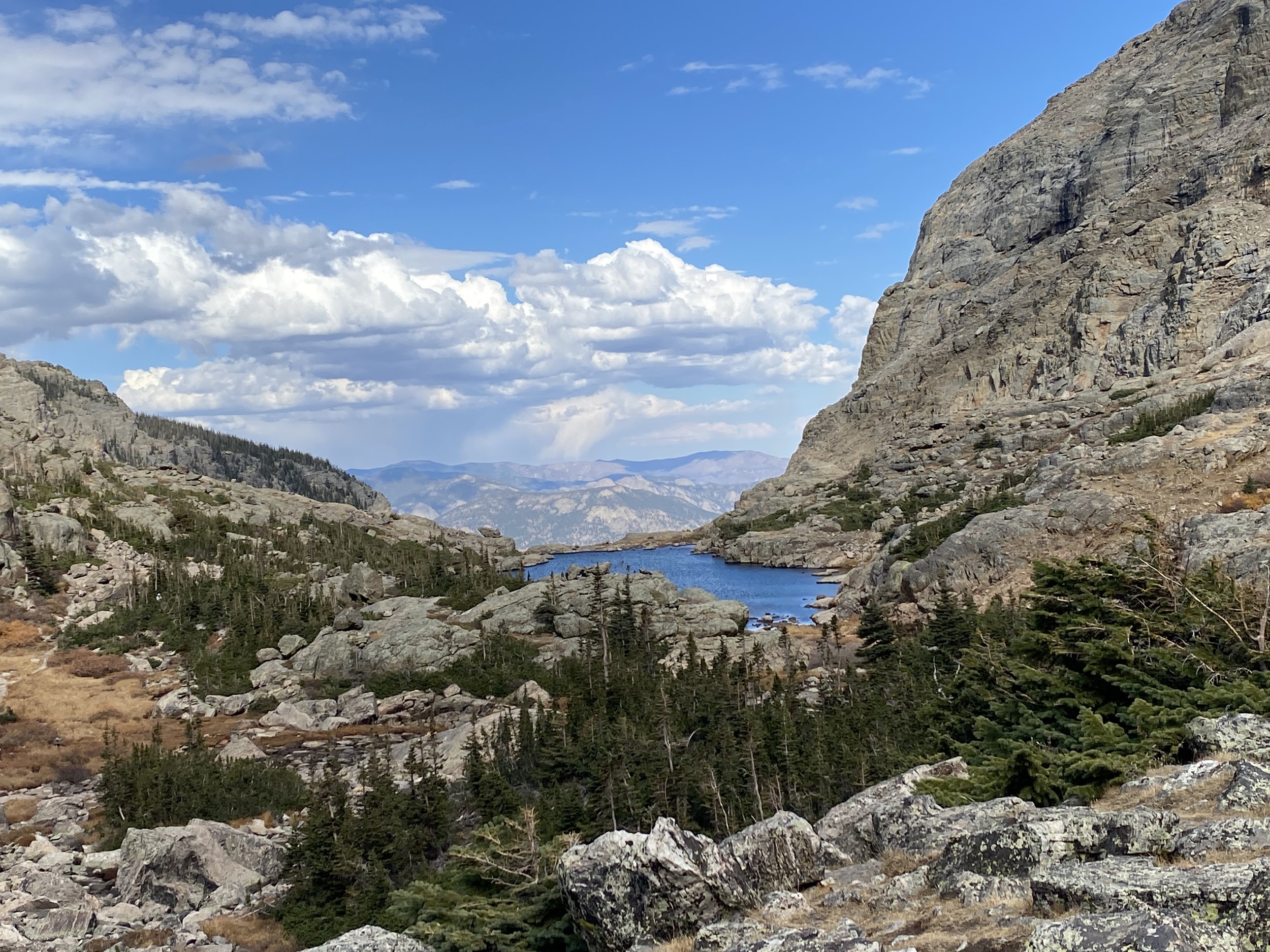 A mountain landscape featuring rocky cliffs, a river, and a partly cloudy sky.