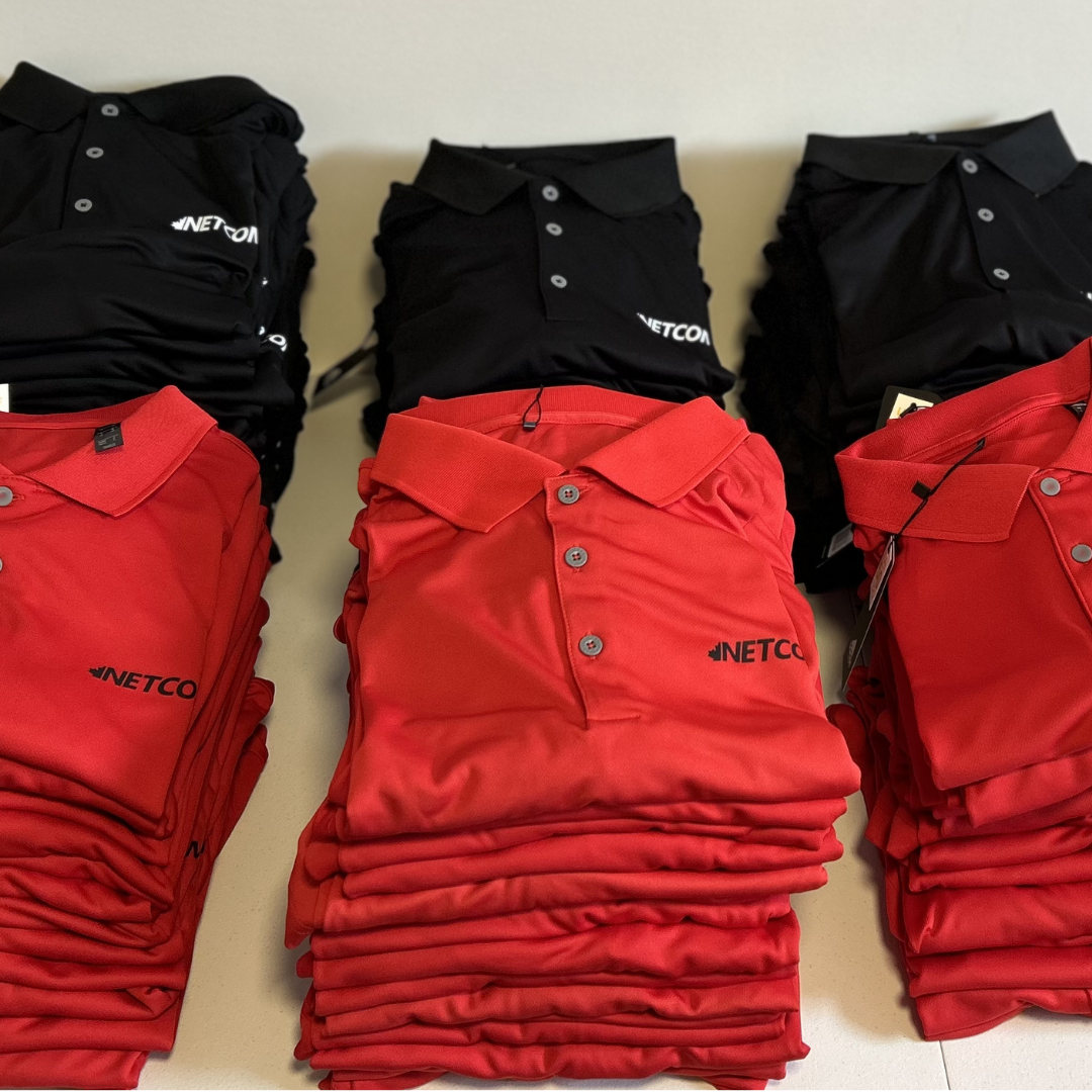 Stacks of red and black polo shirts with the company logo 'NETCON' on them, arranged on a flat surface.