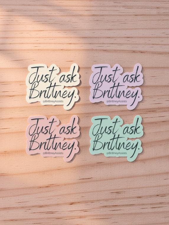 Four colorful stickers with the phrase "Just ask Brittany" in cursive on a wooden surface.