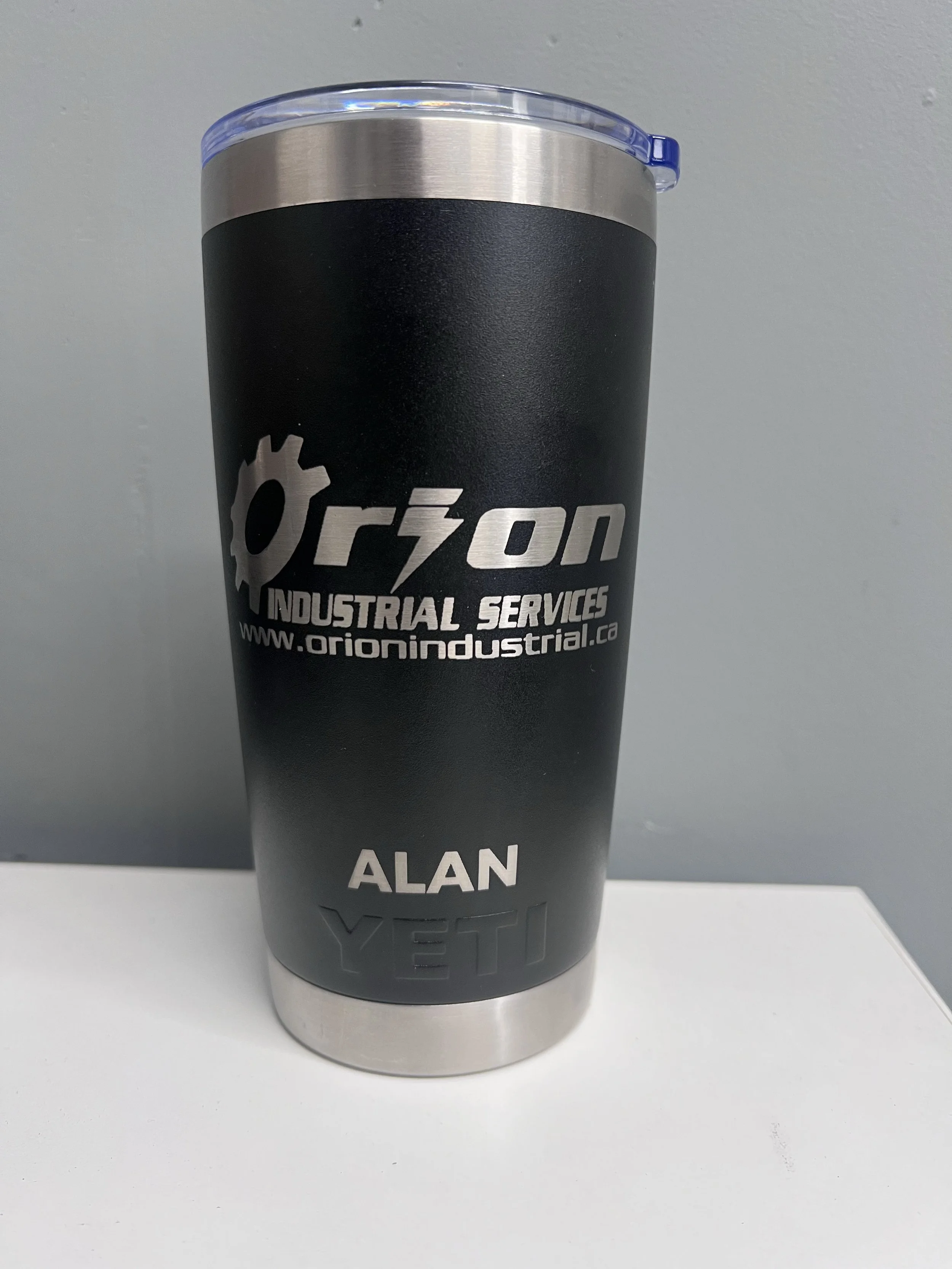 A black travel tumbler with a silver top and a clear lid, featuring the Orion Industrial Services logo and website, along with the name "ALAN" printed in white.