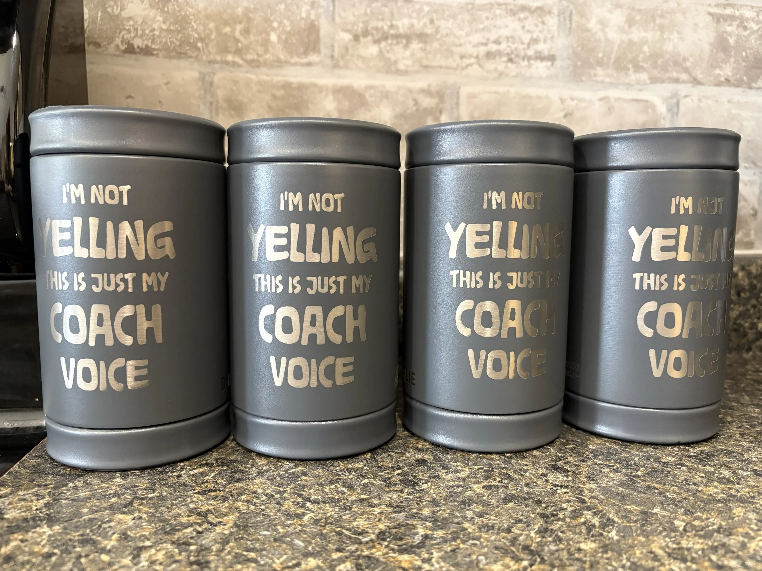 Gray insulated travel mug with motivational quote in white and gold lettering, placed on a kitchen countertop.