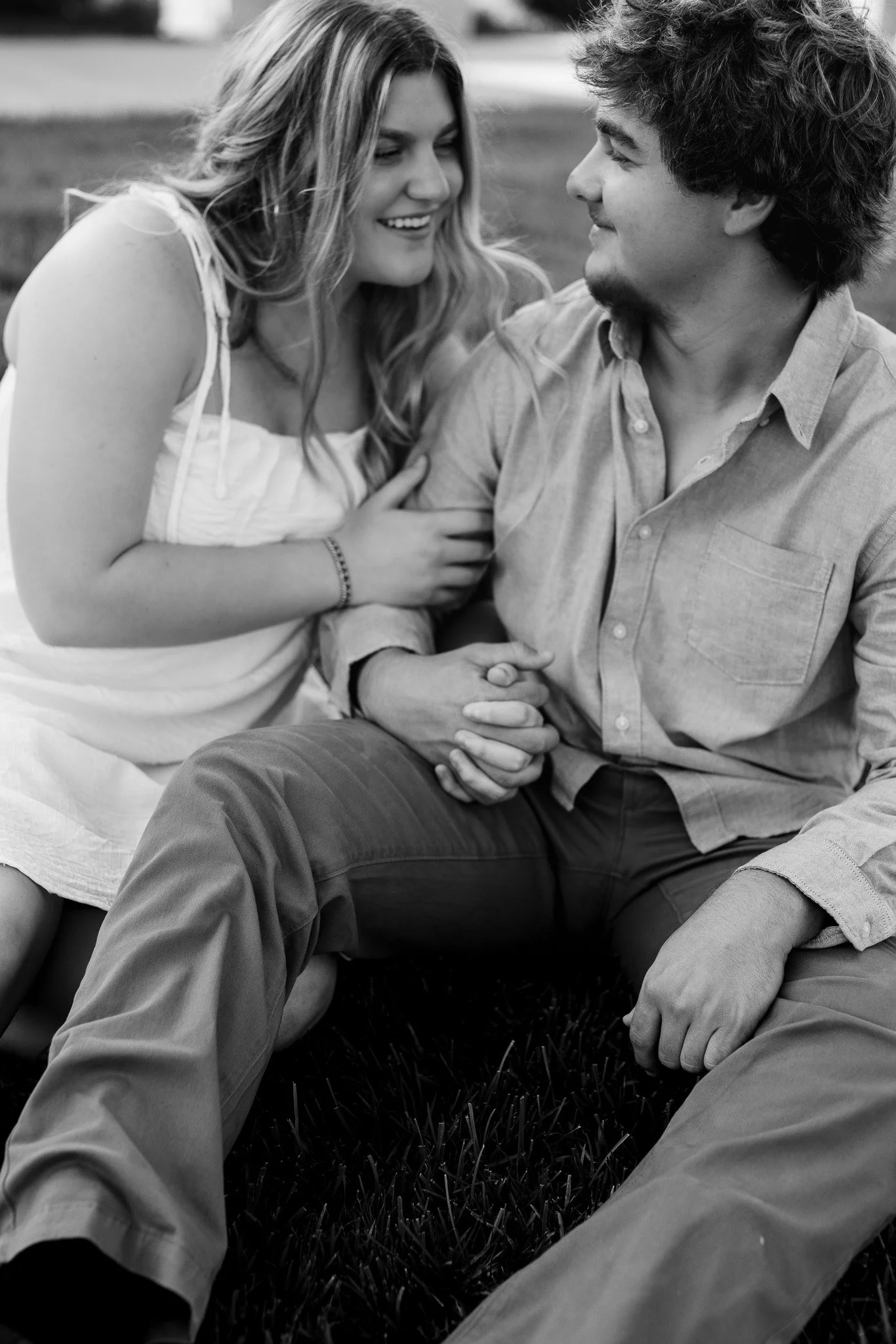 A young couple sitting on the grass, smiling at each other, in black and white.
