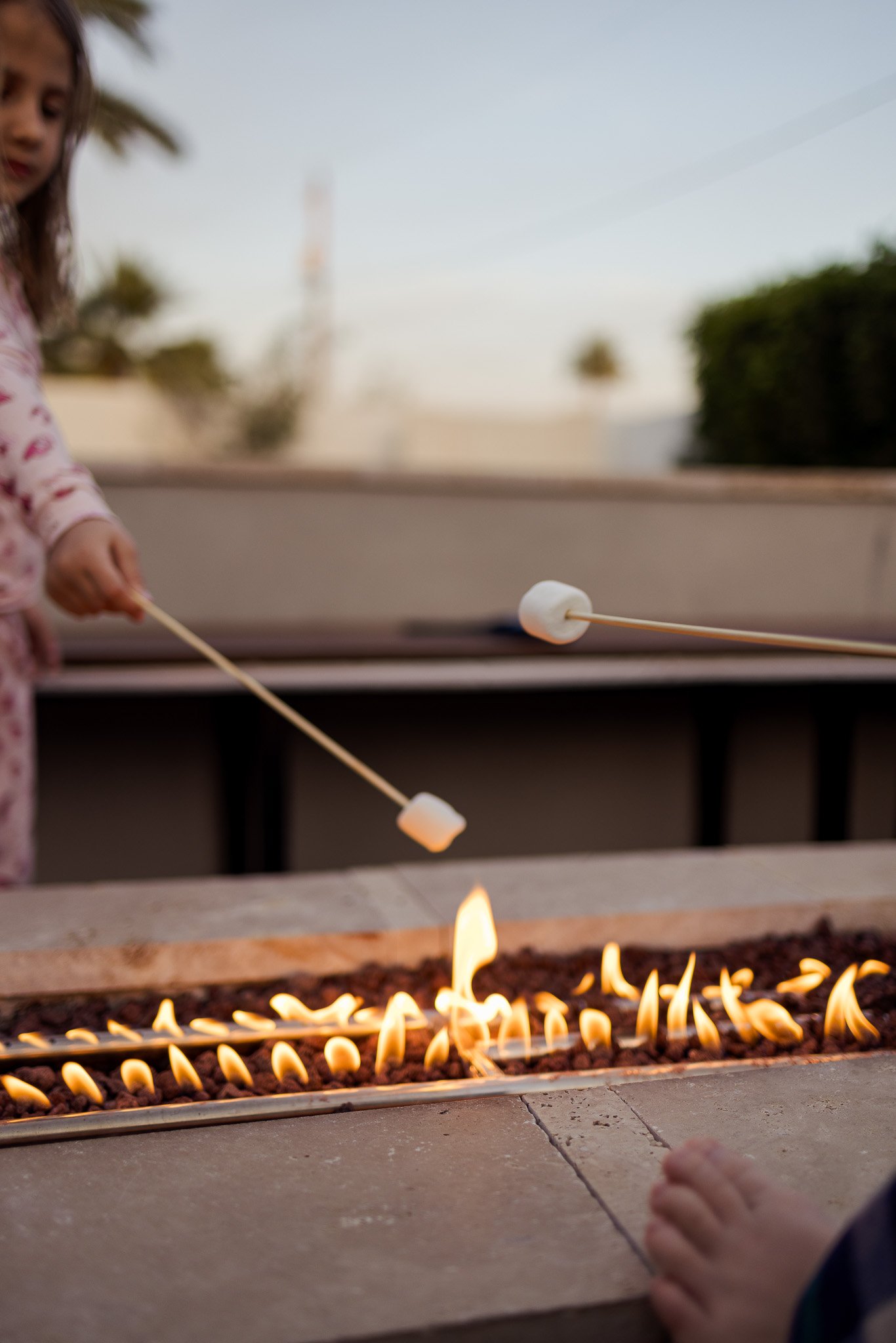 Three children roasting marshmallows over an outdoor fire pit during dusk.