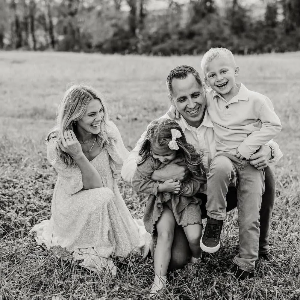 A happy family of five playing outdoors in a grassy field, smiling and laughing together.