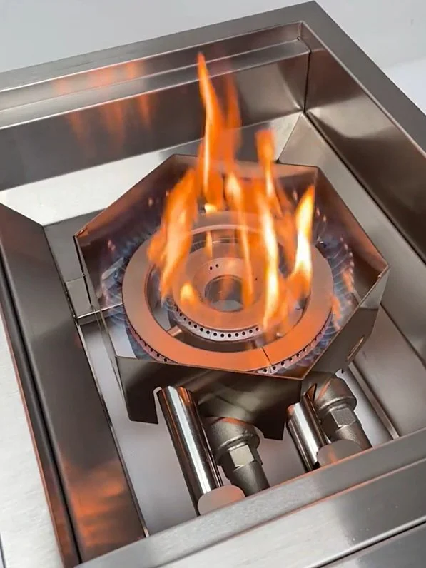 A close-up of a gas stove burner with flames, surrounded by a stainless steel cooking surface.
