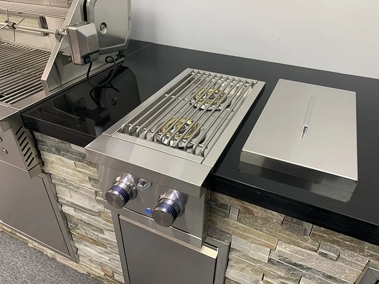 A commercial kitchen countertop with a gas grill, a grill cover, and a stone-tile wall.