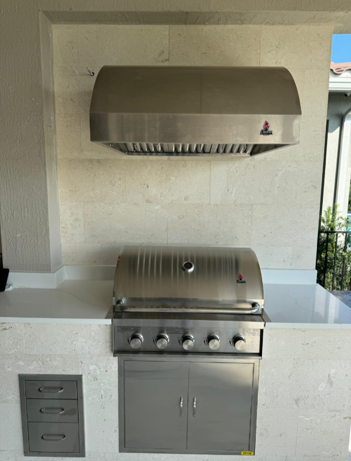 Stainless steel outdoor grill with hood and side cabinet on a stone countertop.