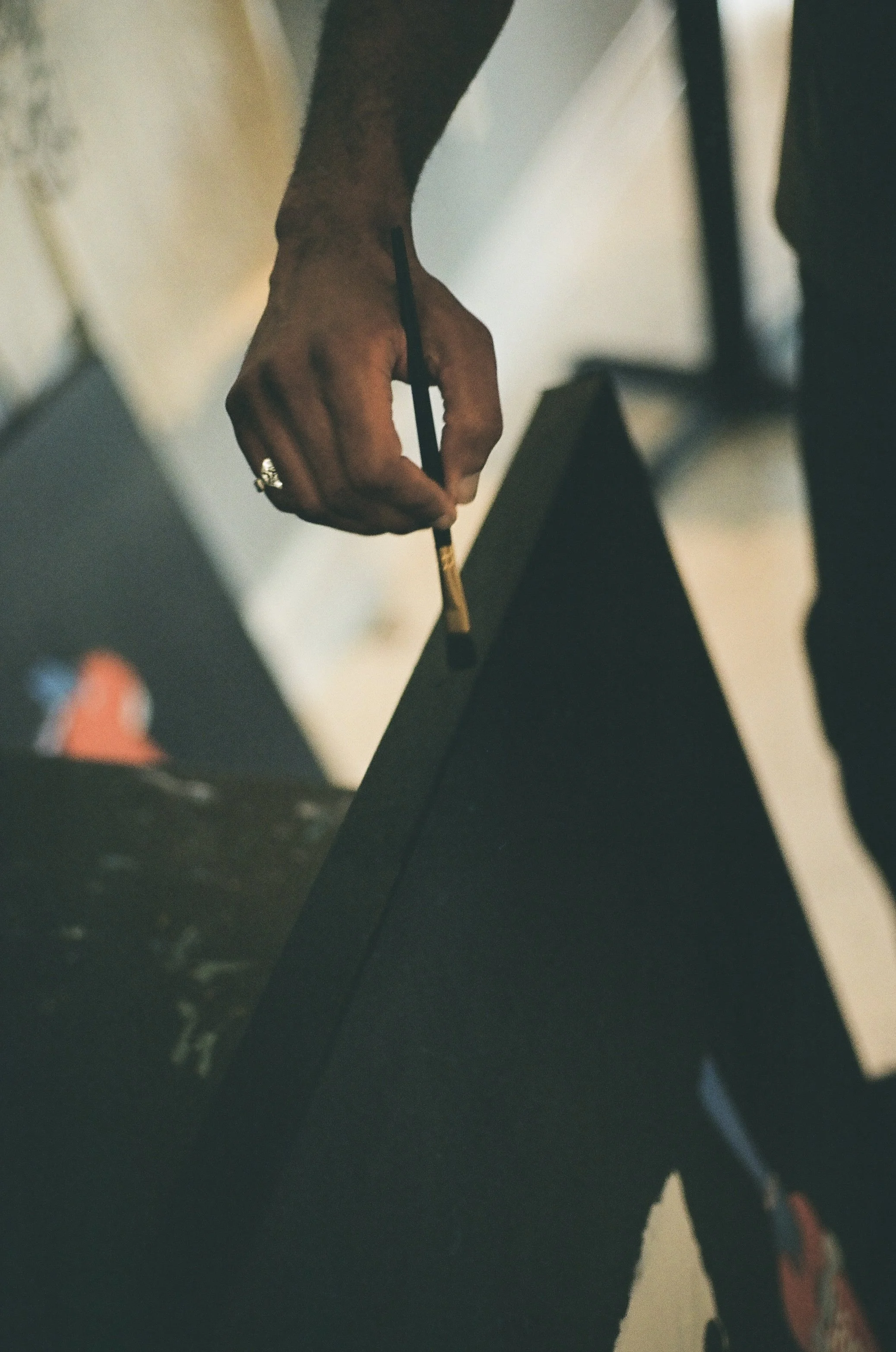 Close-up of a hand gripping a black marker, resting on a dark table or keyboard, with background elements blurred.
