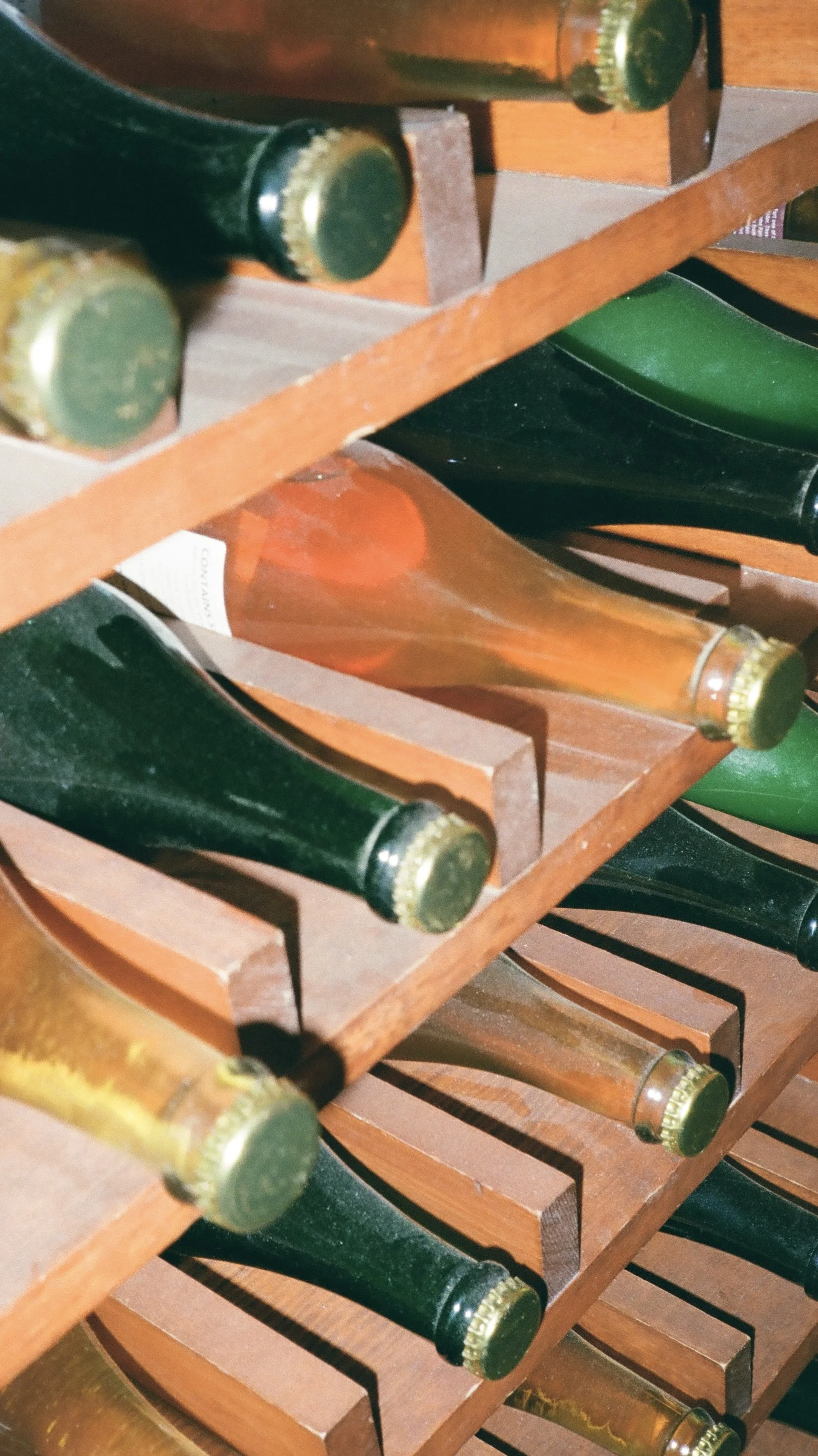Multiple wine bottles stored horizontally in wooden wine racks.
