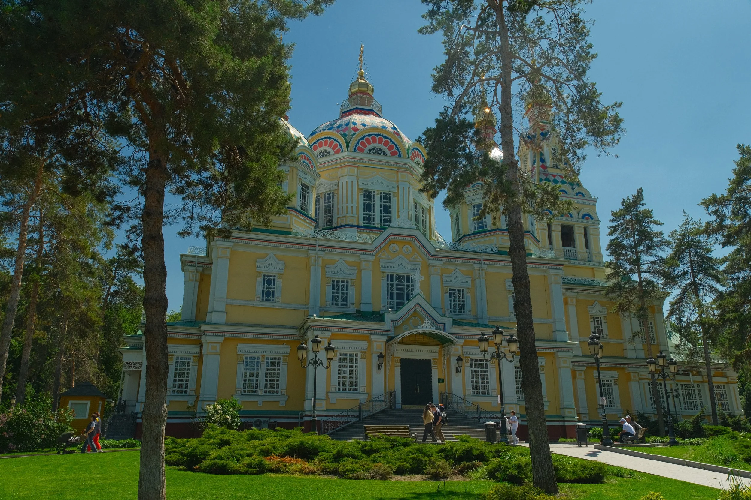 Ornate yellow facade and colorful onion domes of Ascension Cathedral surrounded by pine trees, Almaty, Kazakhstan