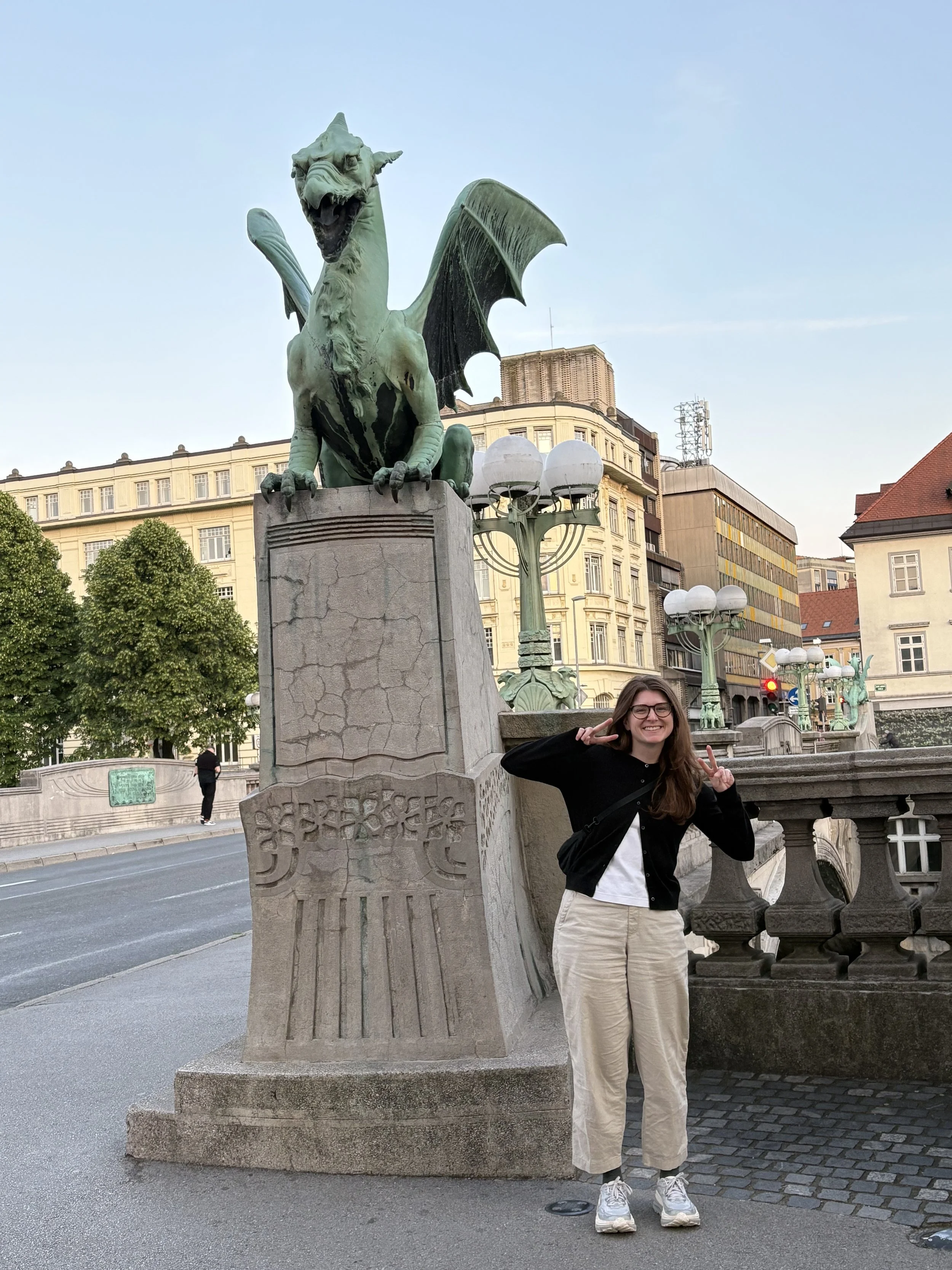 Woman posing beside one of the copper dragon statues on Ljubljana's Dragon Bridge, Slovenia
