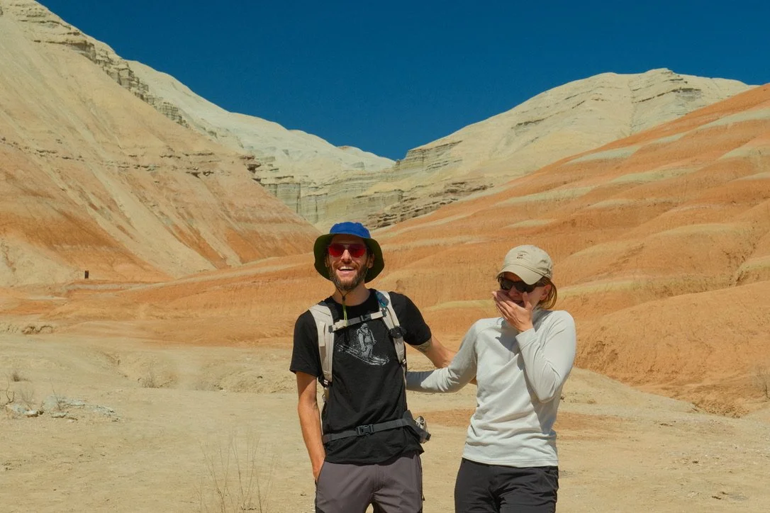 Couple laughing in front of the striped sedimentary Aktau Mountains at Altyn-Emel National Park, Kazakhstan