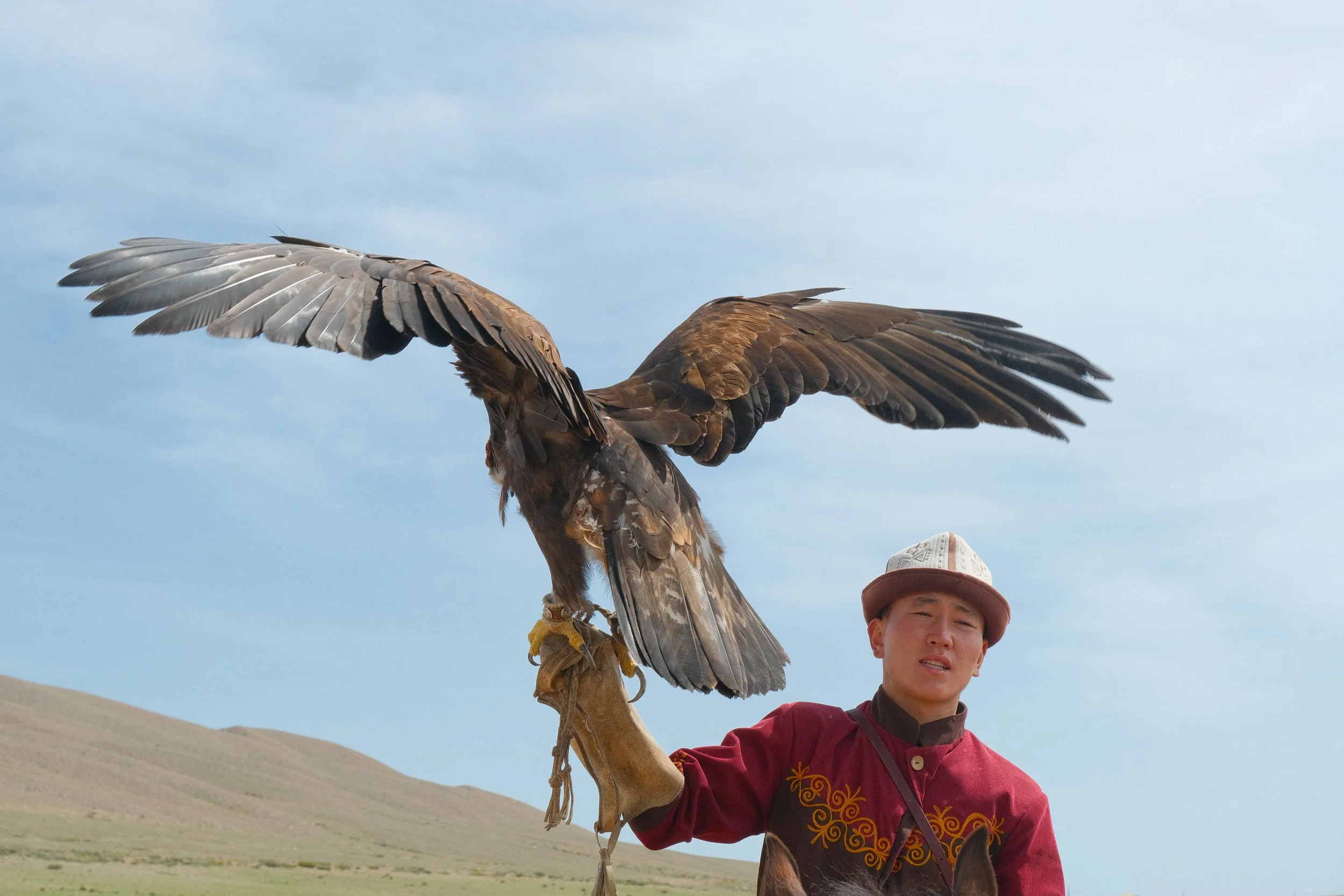 Eagle hunter in a traditional white kalpak holding a golden eagle with wings spread in Kyrgyzstan
