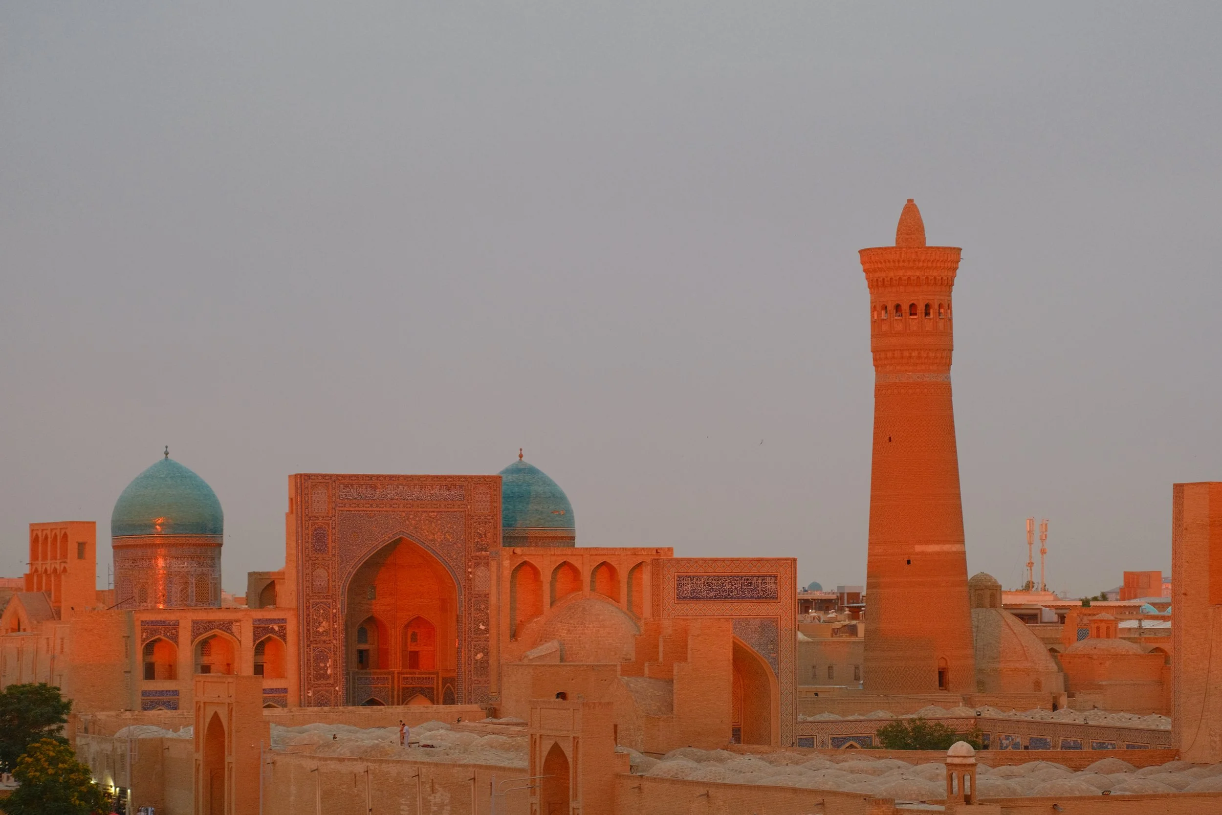 Po-i-Kalon complex at golden hour viewed from the Ark fortress, Kalon Minaret and Mir-i-Arab Madrassa turquoise domes glowing in warm evening light, Bukhara, Uzbekistan