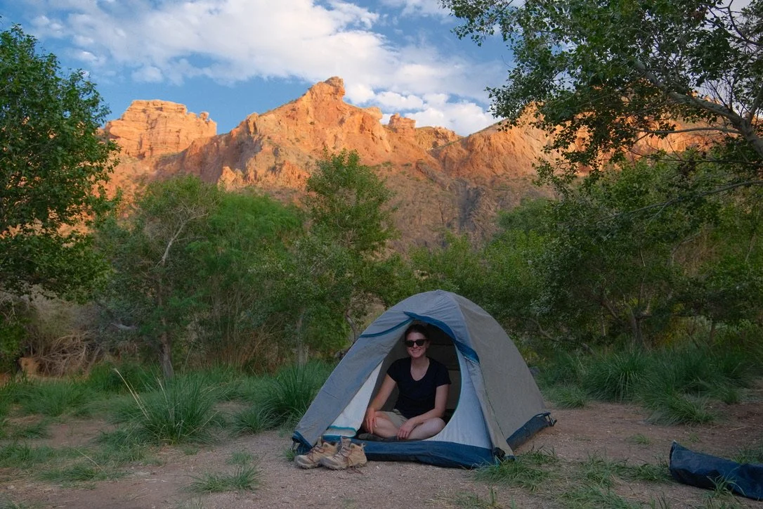 Traveler sitting in a tent at the bottom of Charyn Canyon with red sandstone cliffs glowing at sunset, Kazakhstan
