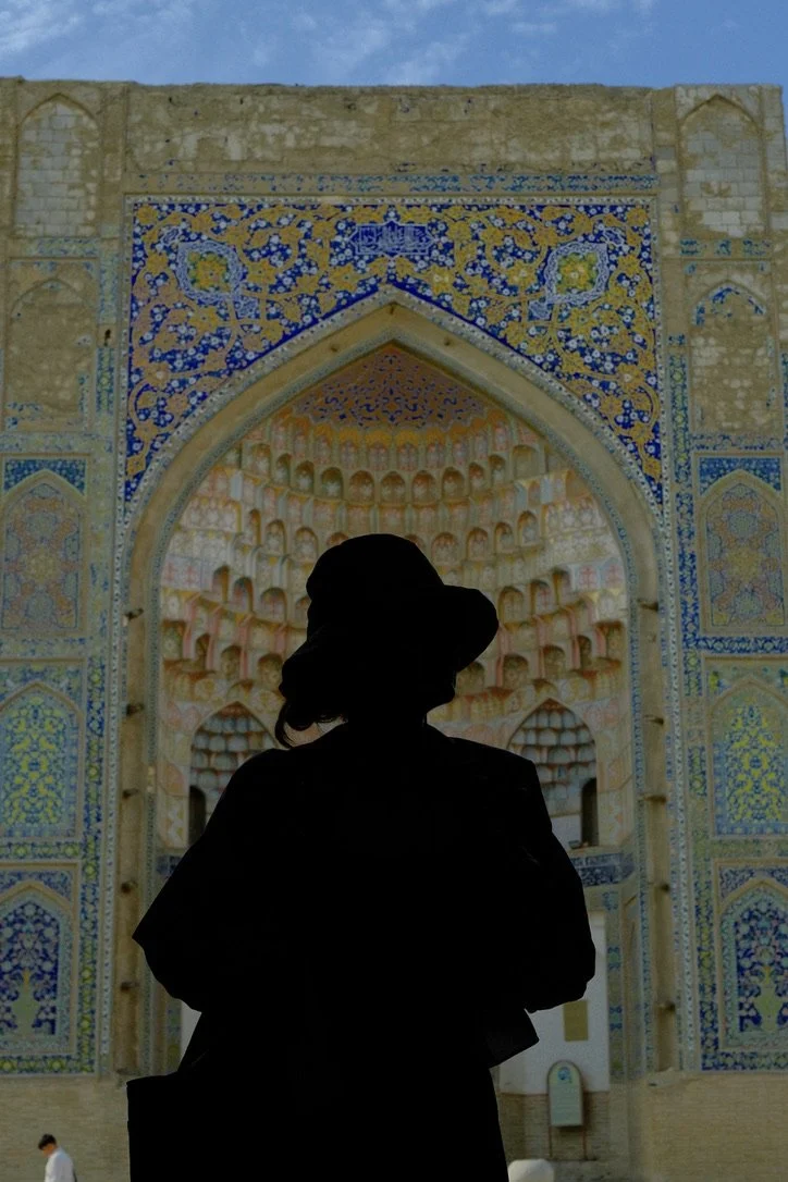 Silhouette of a woman in a hat standing before the ornate muqarnas iwan entrance of Abdulaziz Khan Madrassa, Bukhara, Uzbekistan