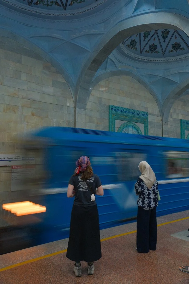 Two women watching a blue metro train pass through the ornate arched interior of Alisher Navoi metro station, Tashkent, Uzbekistan