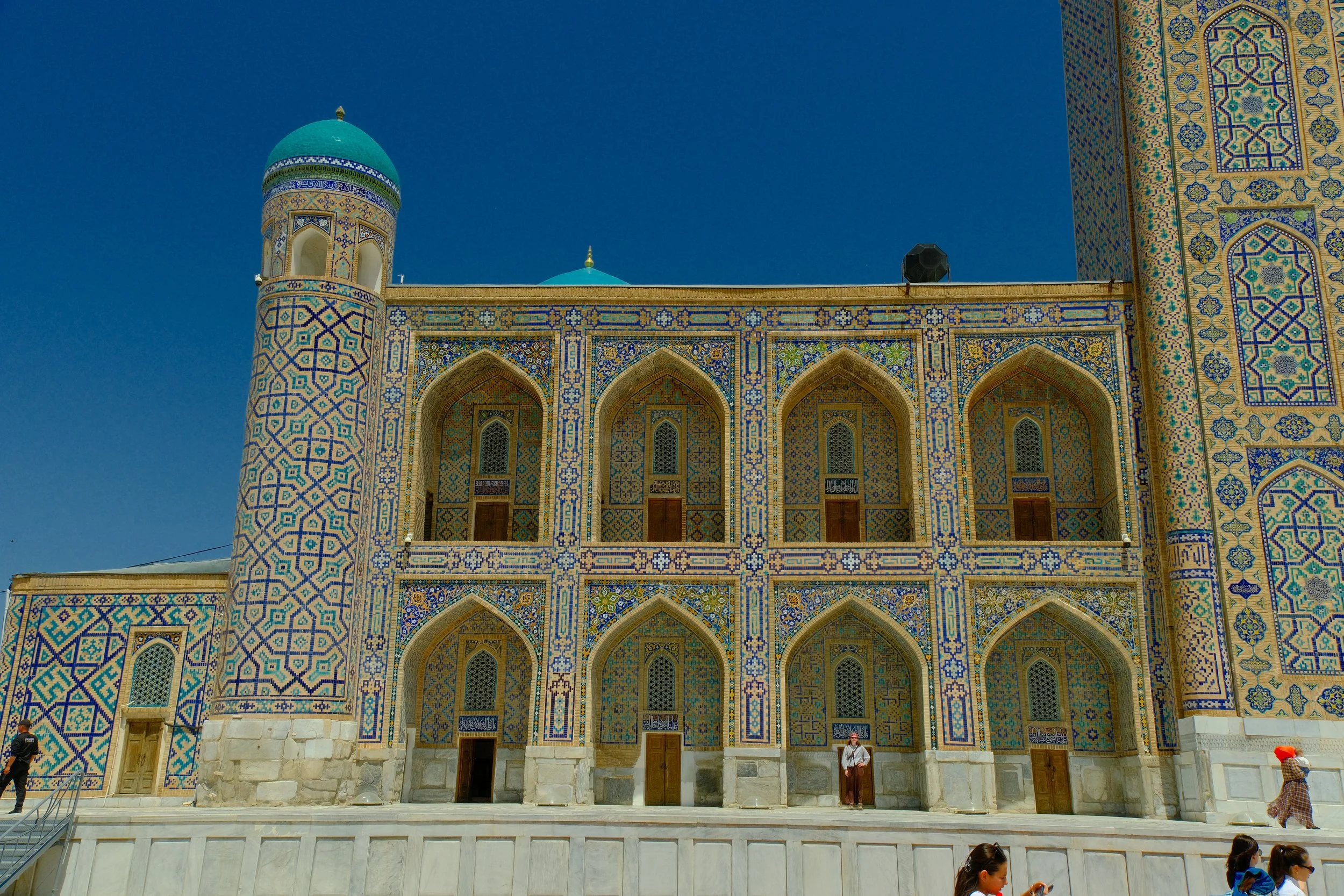 Ornate geometric tilework facade and arched niches of Tilya-Kori Madrassa courtyard with turquoise dome, Registan Square, Samarkand, Uzbekistan
