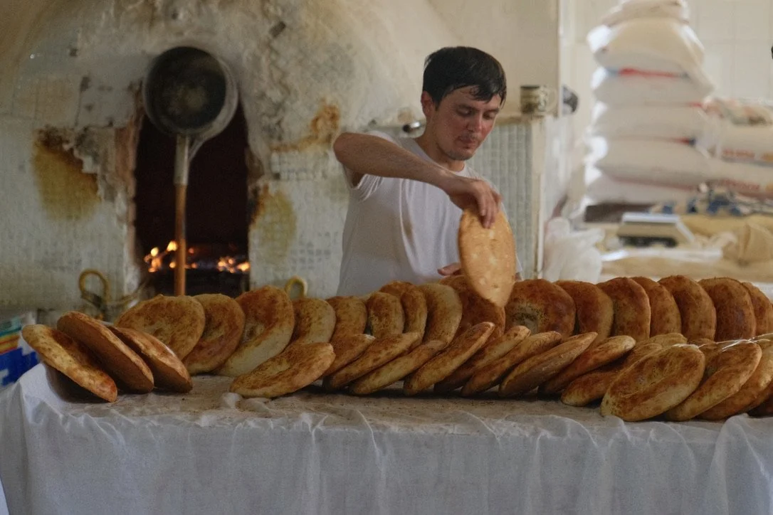Baker arranging freshly baked non flatbread on a display table in front of a traditional tandoor oven at Chorsu Bazaar, Tashkent, Uzbekistan