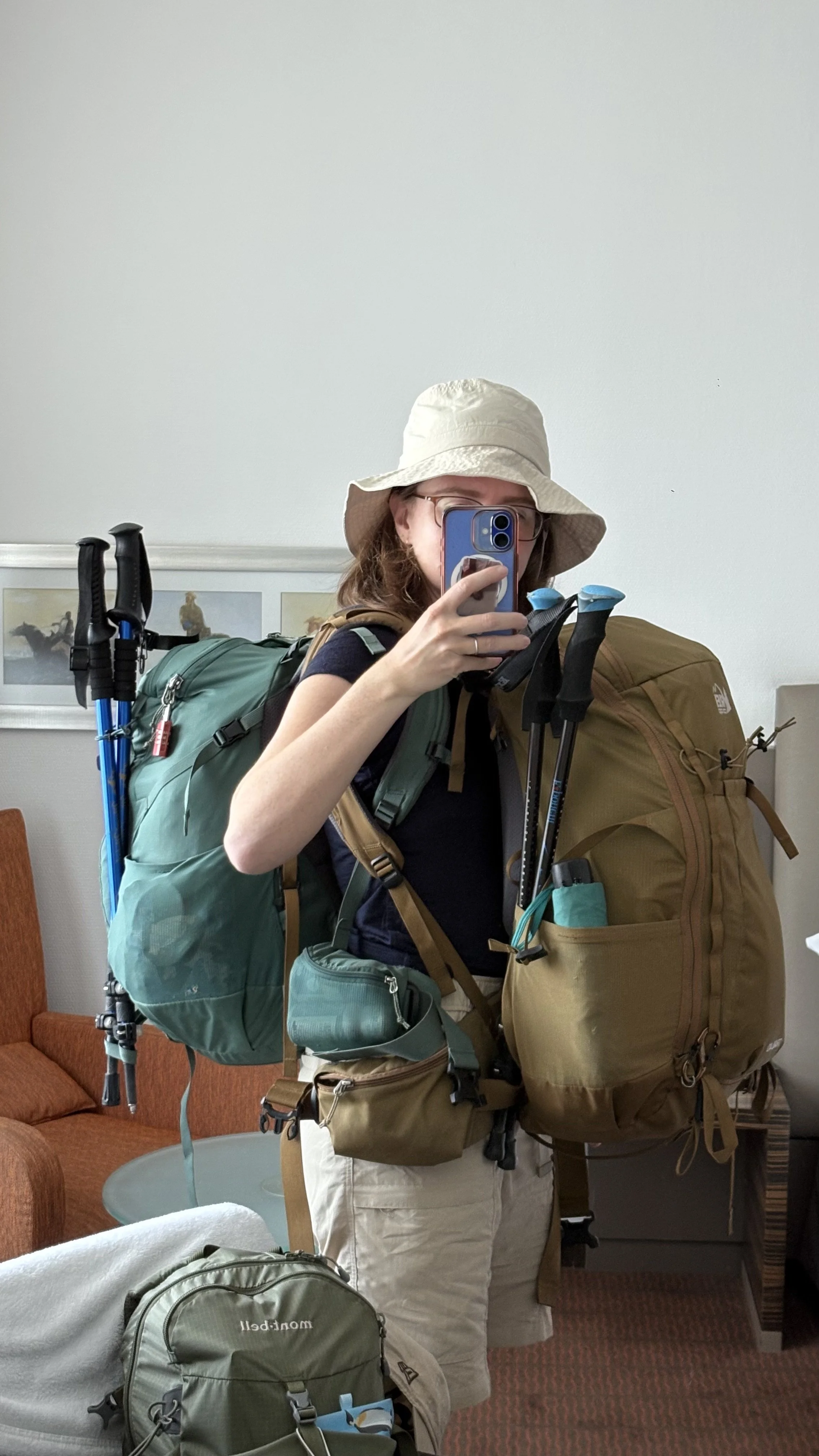 Traveler taking a mirror selfie wearing a daypack and carrying a hiking backpack with trekking poles, ready for one-bag travel