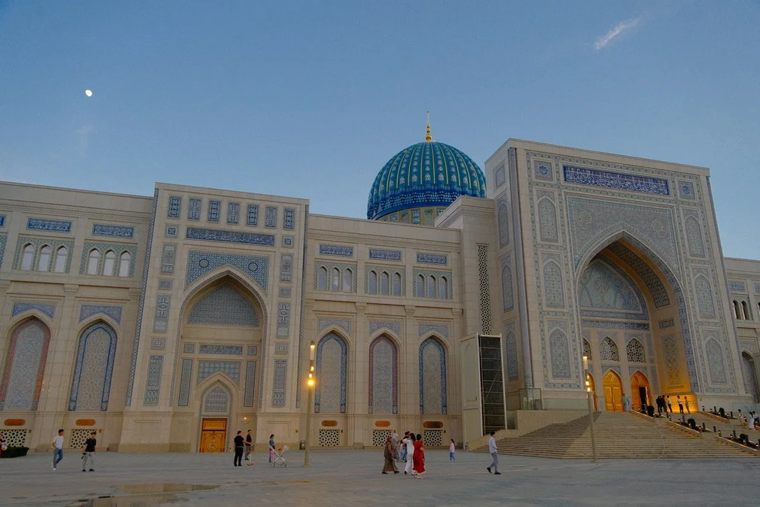Hazrati Imam mosque complex at dusk with turquoise dome, ornate tilework facade, and visitors in the courtyard, Tashkent, Uzbekistan