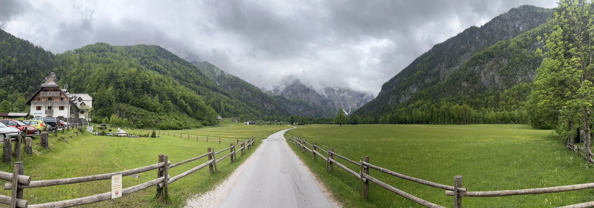 Wooden fence-lined road through Logar Valley with Hotel Plesnik and the Kamnik-Savinja Alps in the background, Slovenia