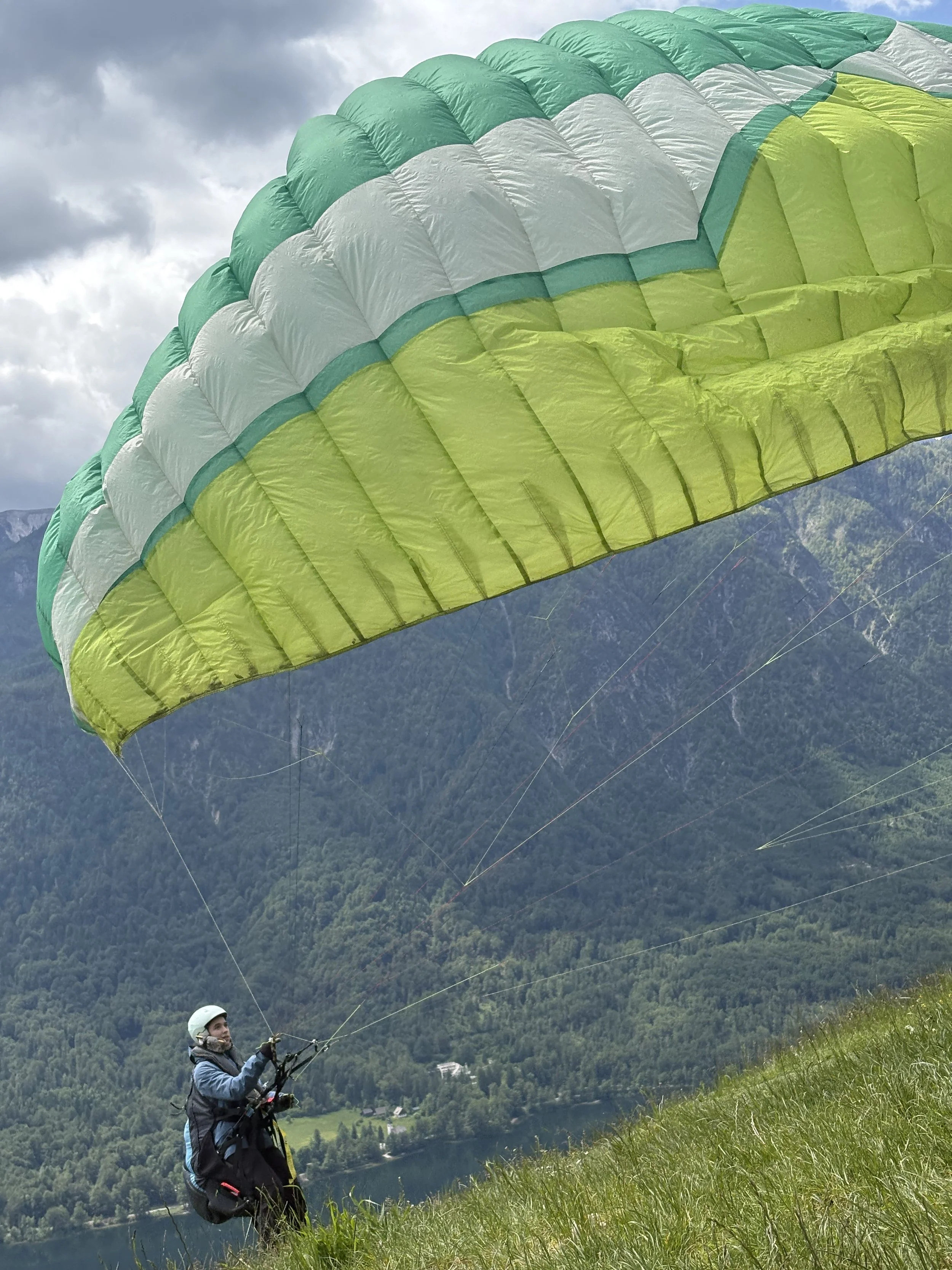 Paraglider launching from a grassy hillside with Lake Bohinj visible in the valley below, Slovenia