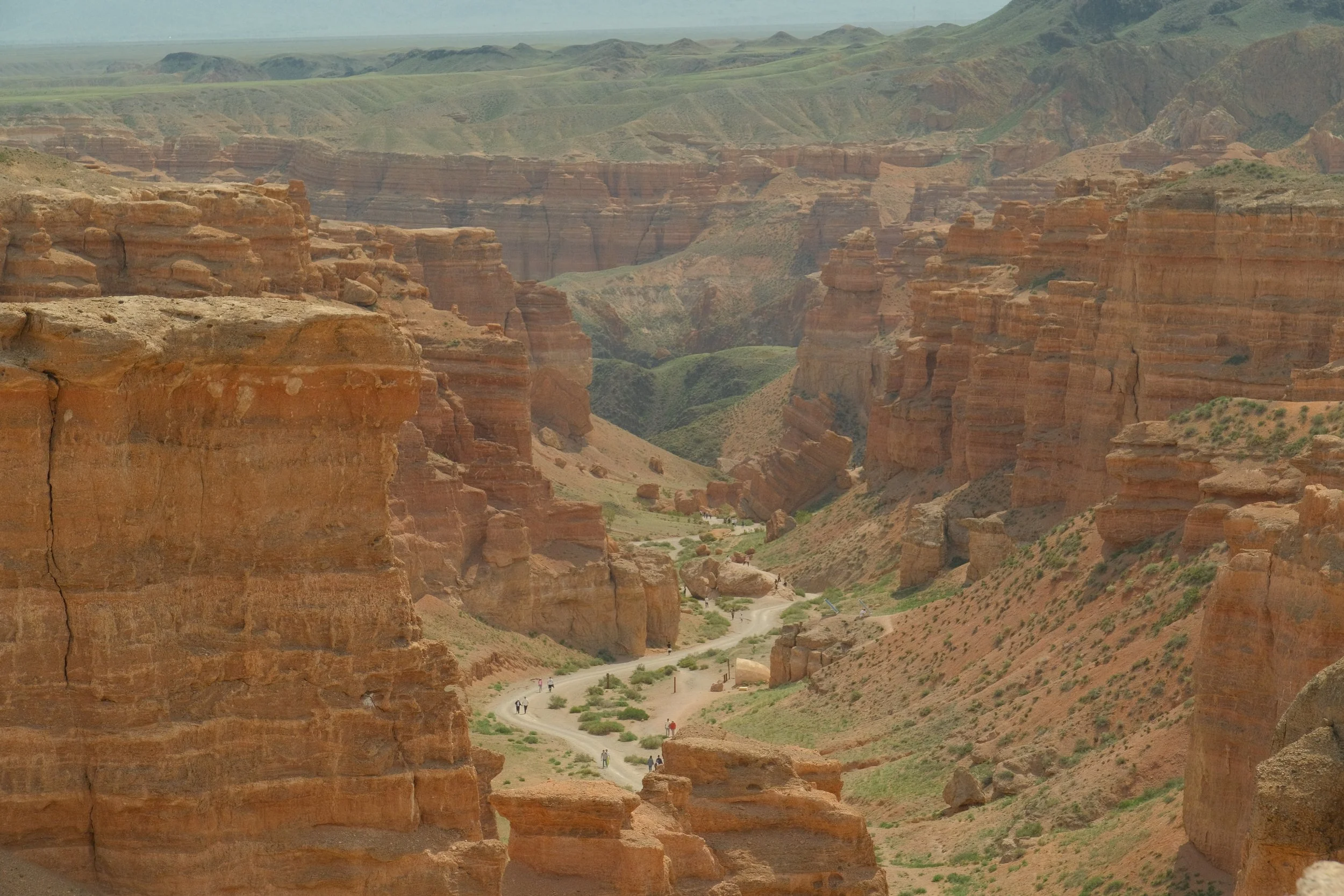 Aerial view of Charyn Canyon's Valley of Castles with dramatic red sandstone formations and hikers on the canyon floor, Kazakhstan