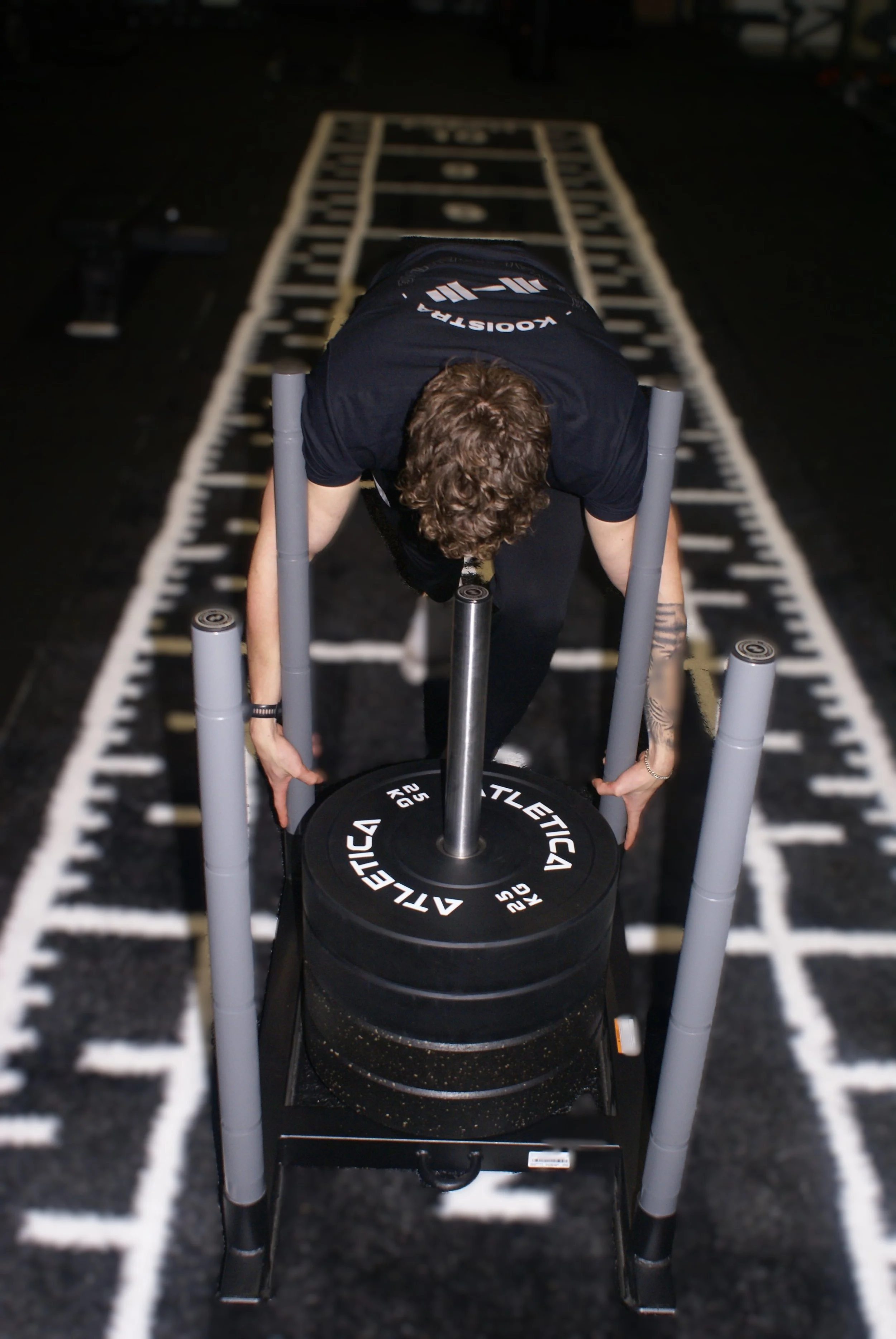 Persoon in sportskleding die gewichten optilt op een fitnessbaan met gewichtplaten en stang.