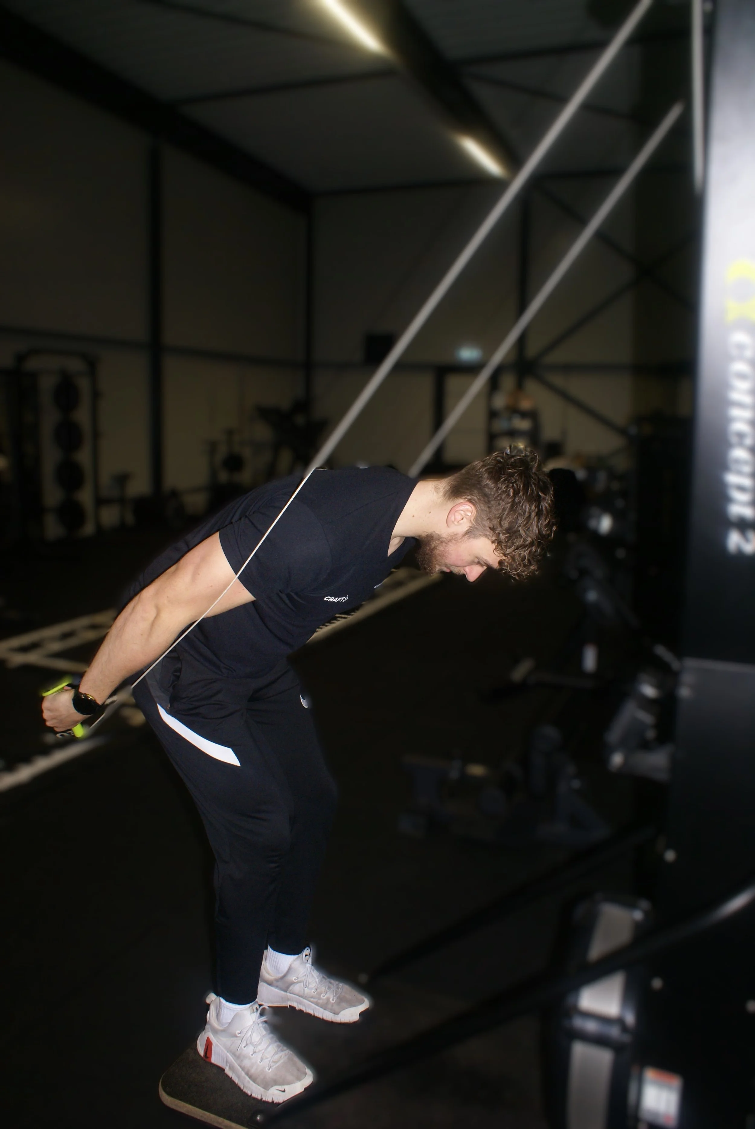 Man in zwart shirt en zwart broek met witte sneakers doet roeitraining in een fitnessruimte.