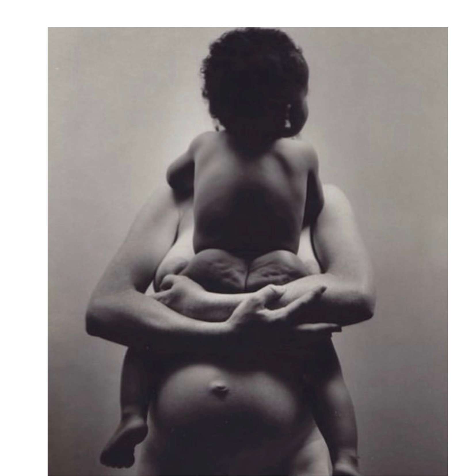 Close-up black and white photograph of a muscular baby doll with hands crossed over chest and curly hair, set against a plain background.