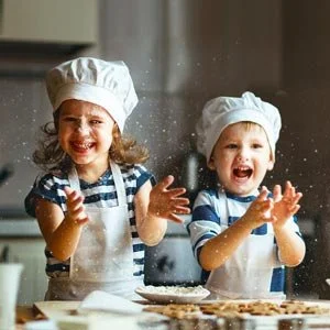 Two children wearing chef hats and aprons baking and having fun in the kitchen.