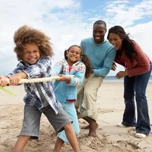 A family of four playing tug-of-war on the beach.