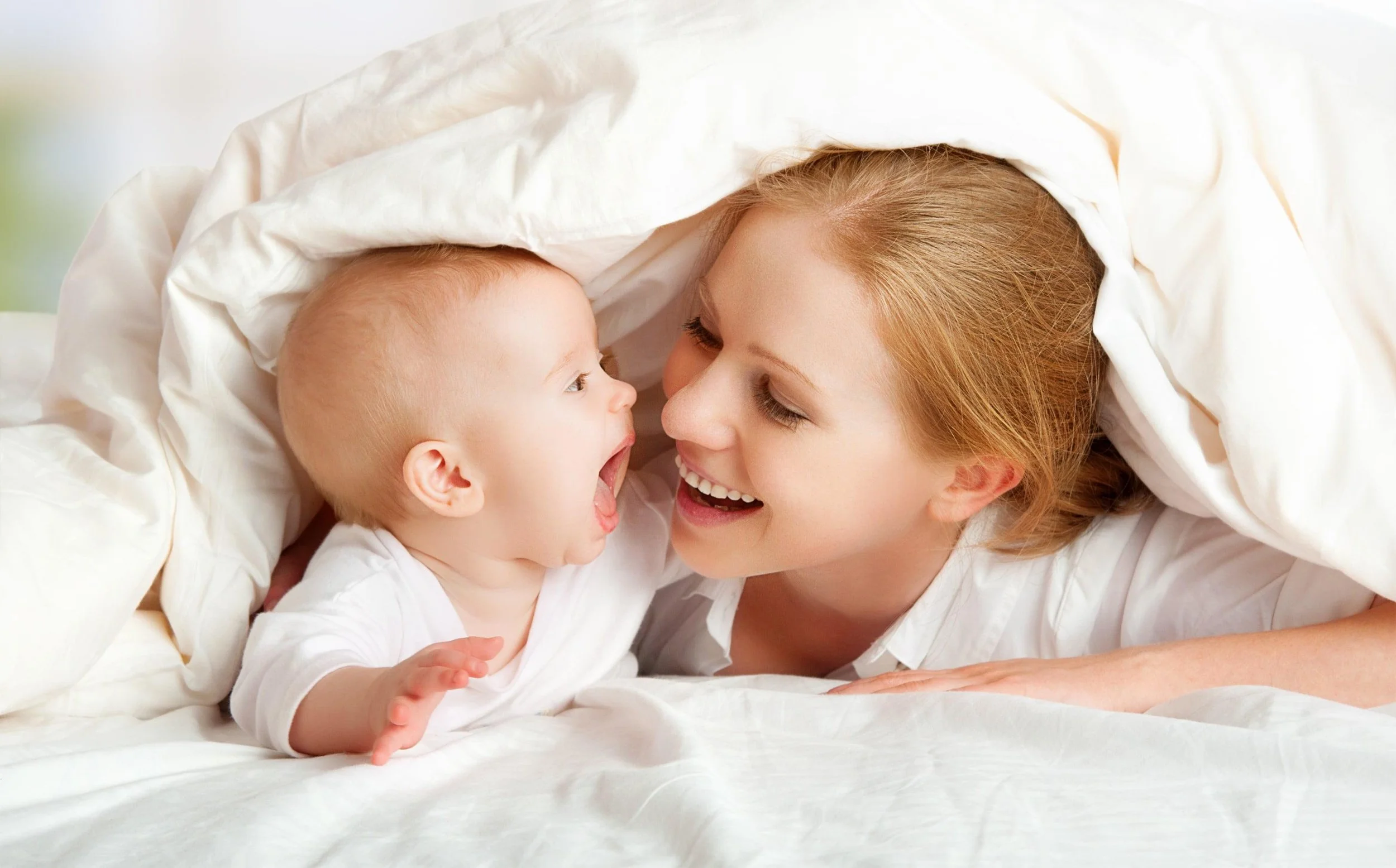 A young woman and a baby sharing a joyful moment under a blanket.