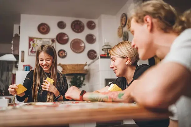 Three people playing a card game at a dining table in a cozy kitchen, smiling and having fun.