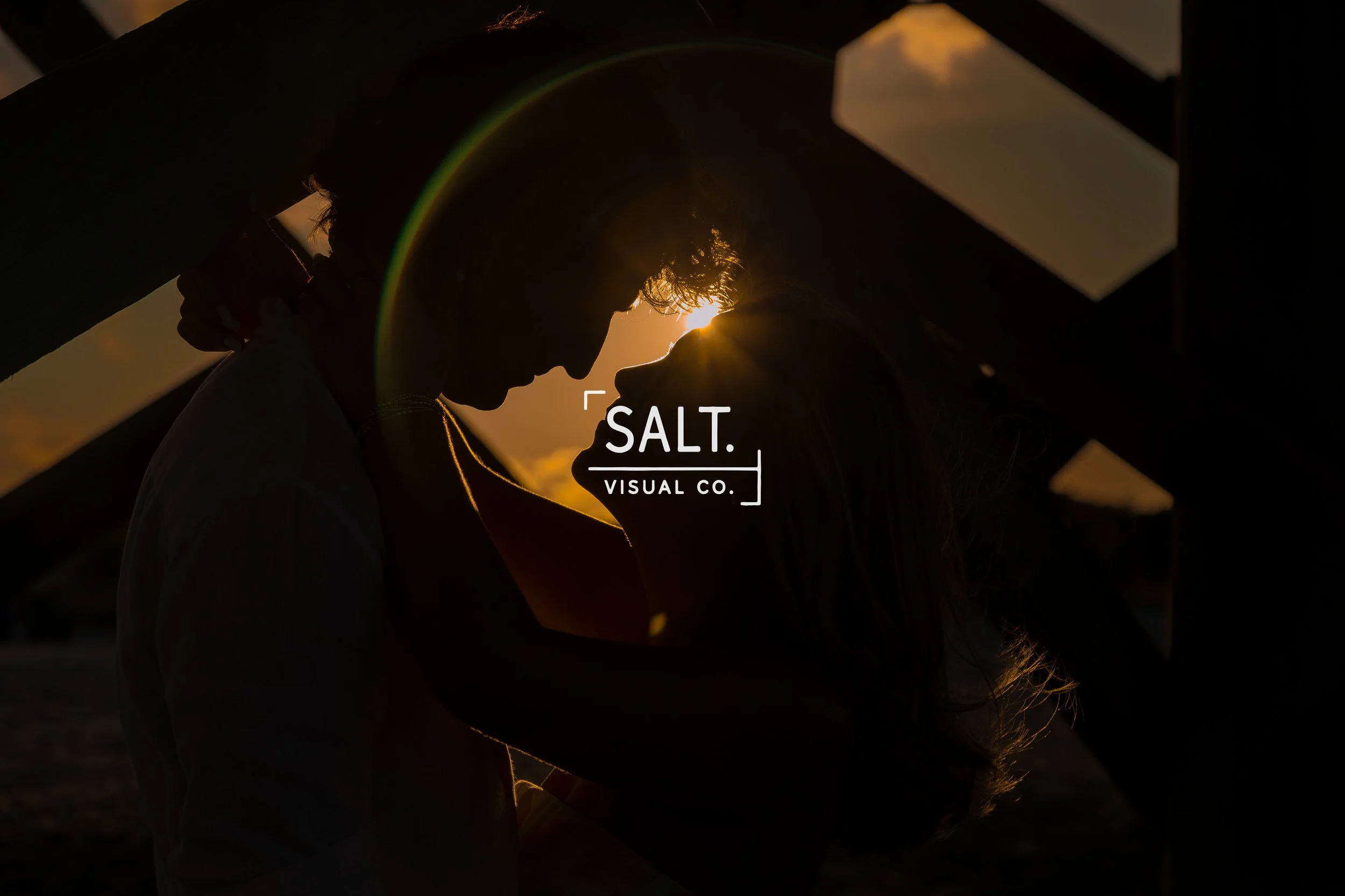 Silhouettes of two people close together with their foreheads touching, backlit by a setting sun, creating a romantic scene.