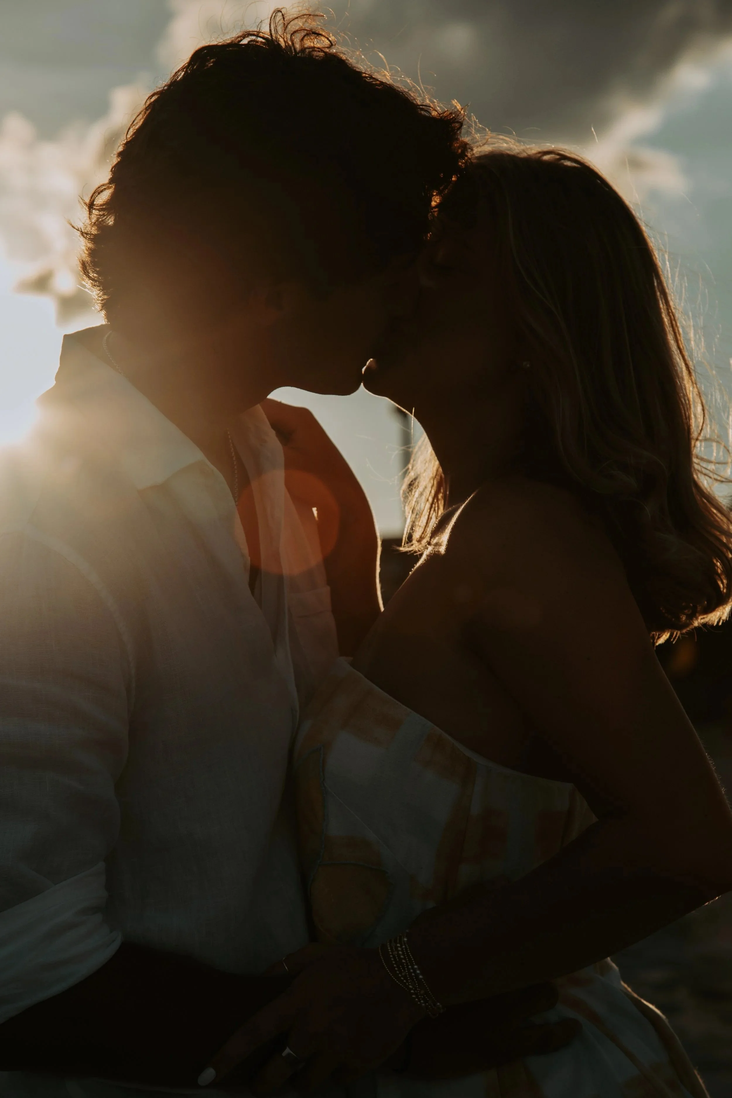 A silhouette of a couple kissing at sunset, with the sunlight creating a backlit glow around them.