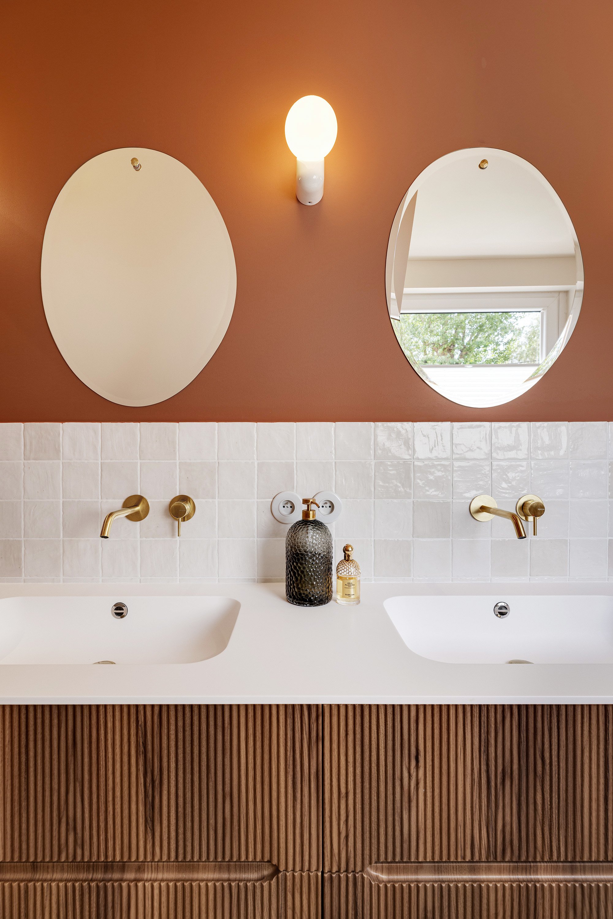 Détail des miroirs ovales, de la robinetterie en laiton et du meuble vasque sur mesure.