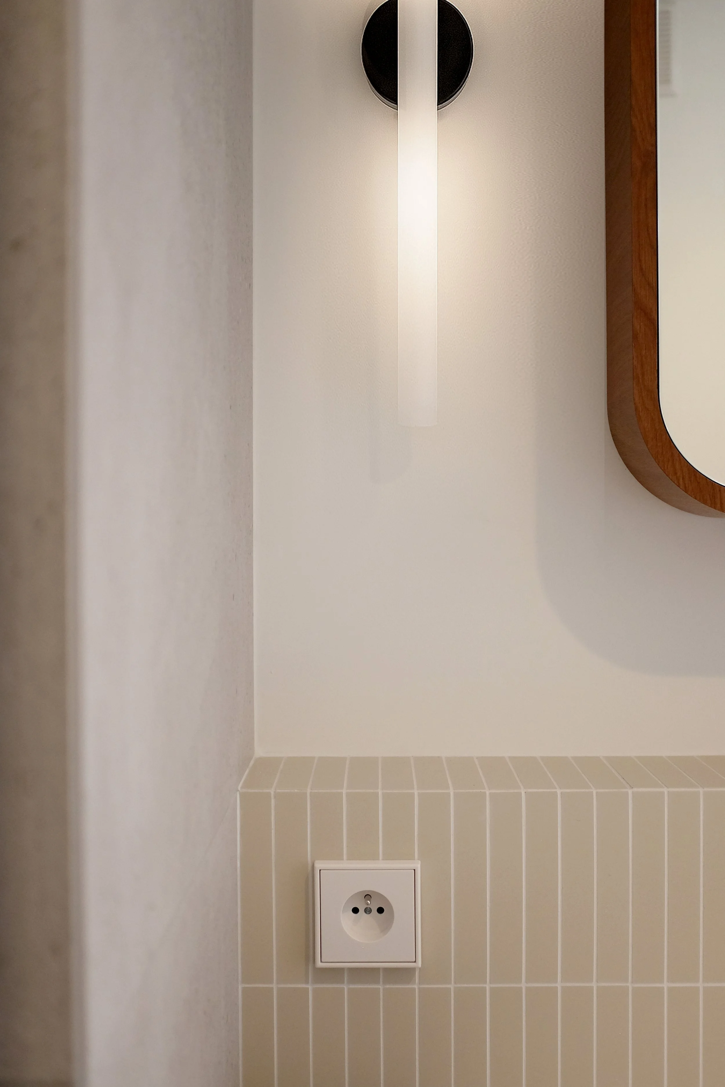 Détail de l'applique murale, de la faïence verticale et des finitions d'une salle de bain rénovée.