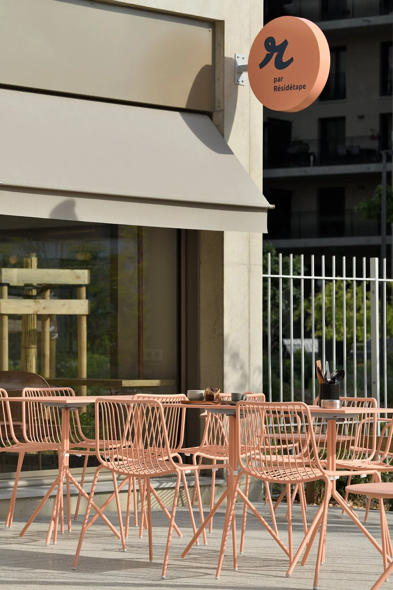 Terrasse d'un café à Lyon avec mobilier extérieur rose et façade contemporaine.