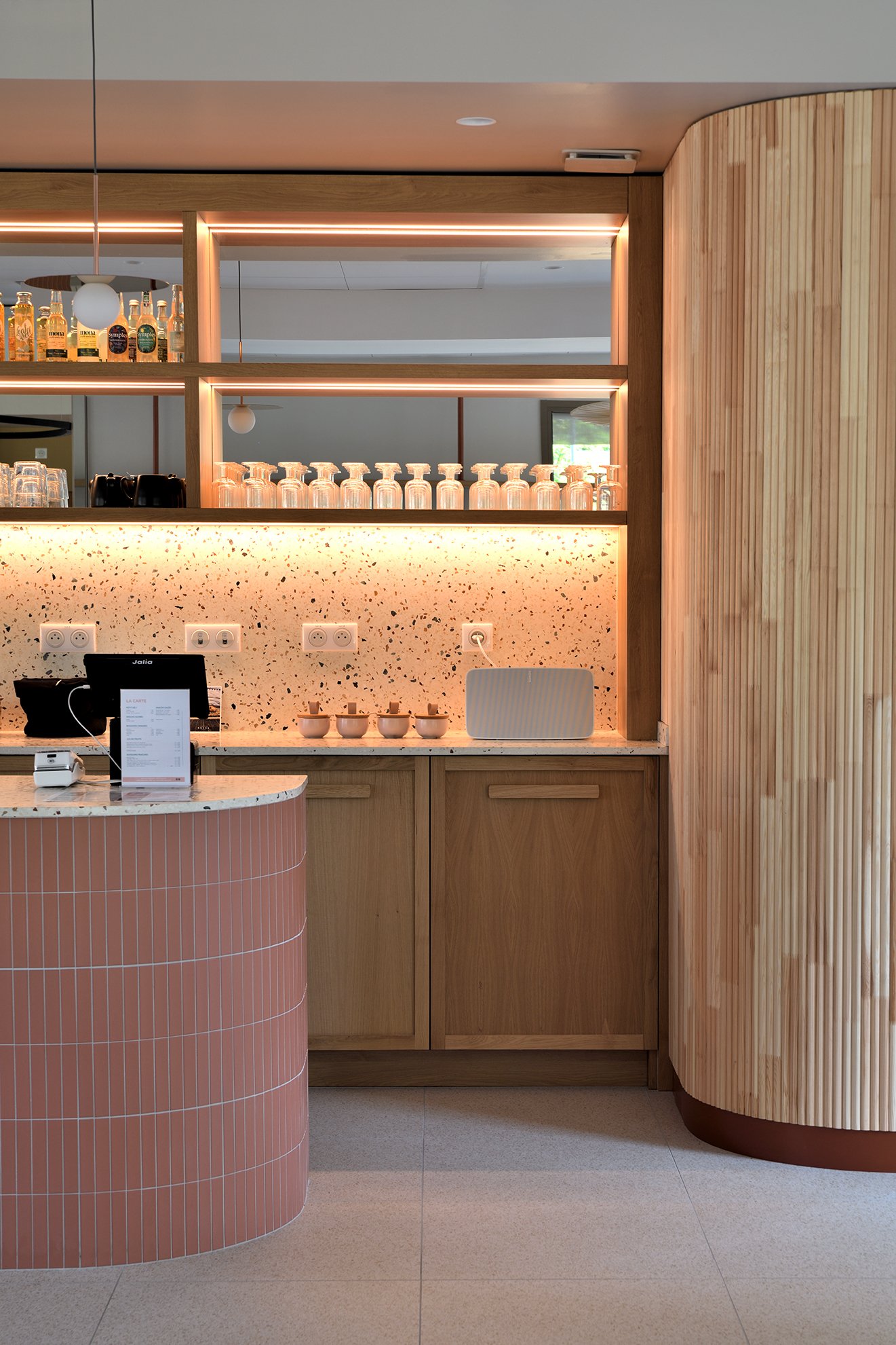 Comptoir de café réalisé sur mesure avec bois, éclairage intégré et crédence en terrazzo.