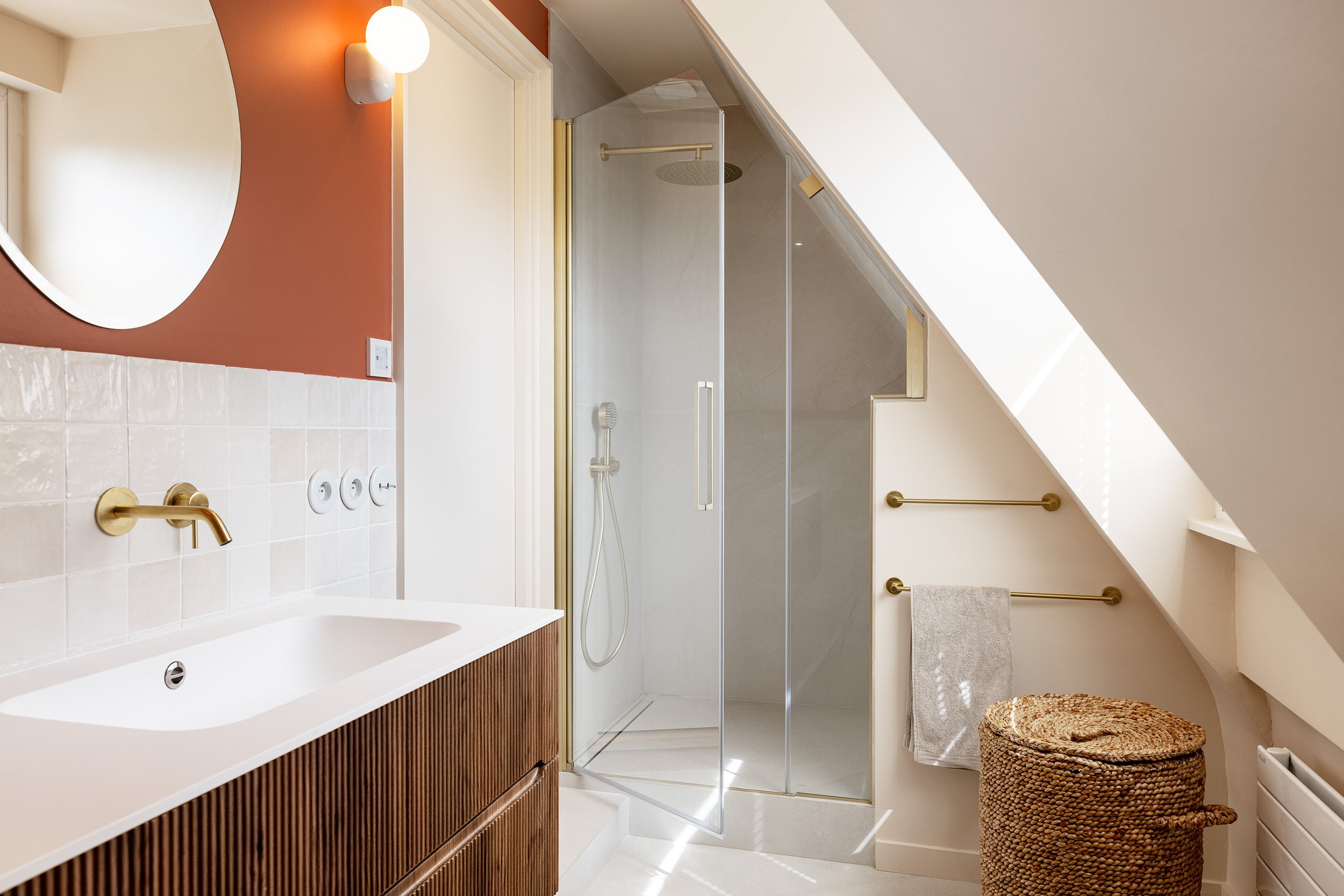 Salle de bain sous combles avec meuble vasque rainuré, douche à l'italienne et finitions en laiton.