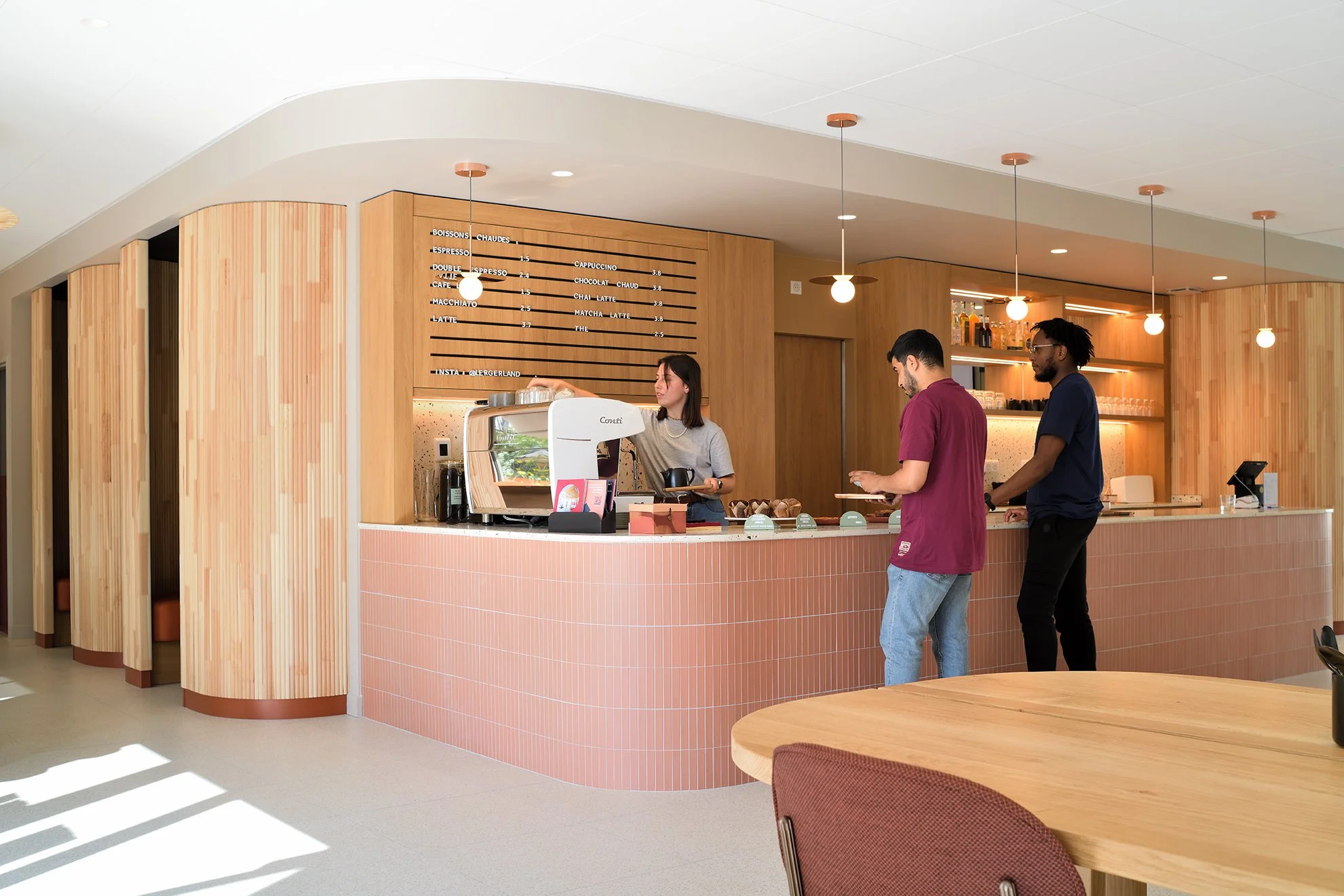 Café et tiers-lieu conçu à Lyon avec comptoir en terrazzo rose, mobilier en bois et agencement sur mesure.