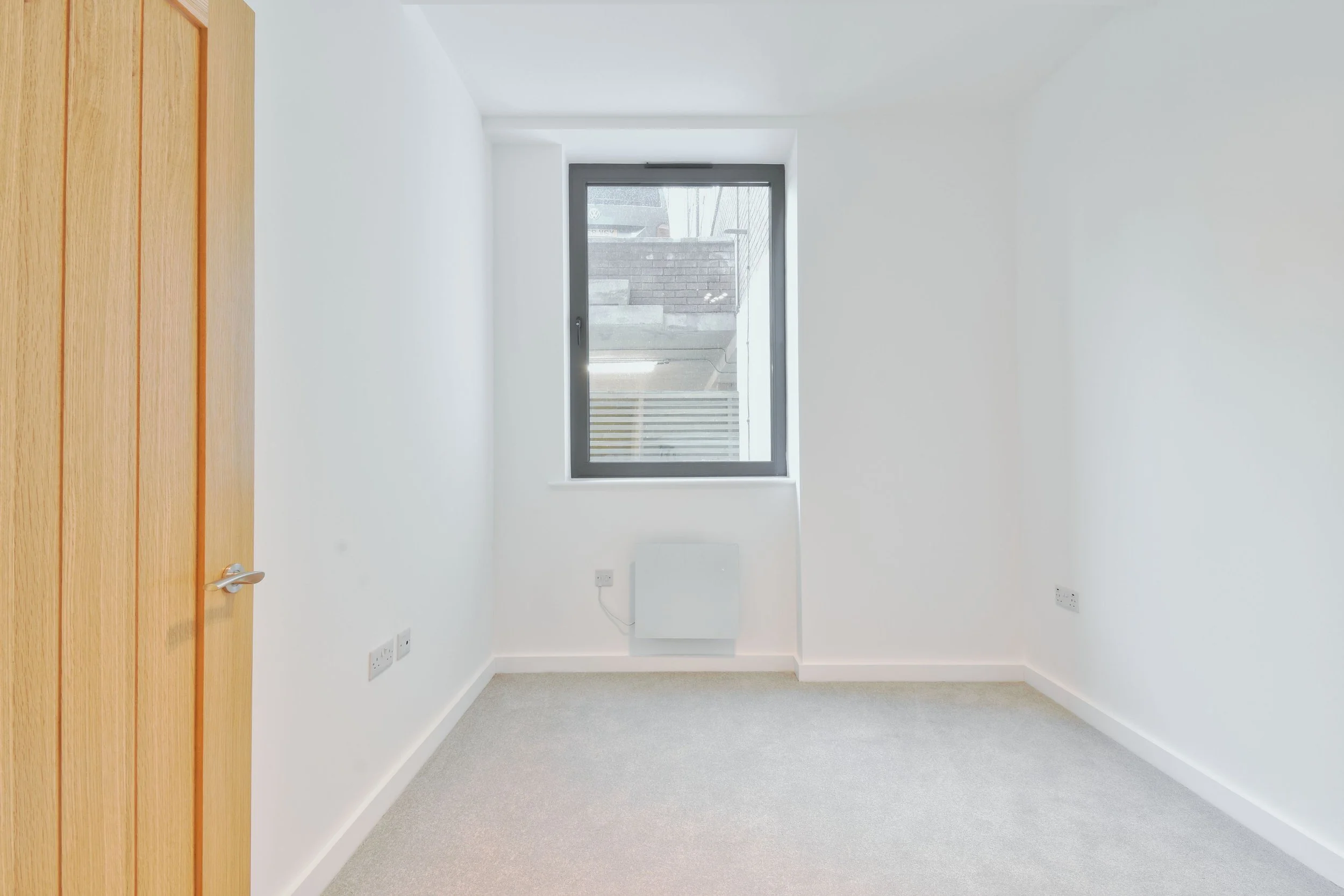 Empty white room with a gray window and a wooden door.