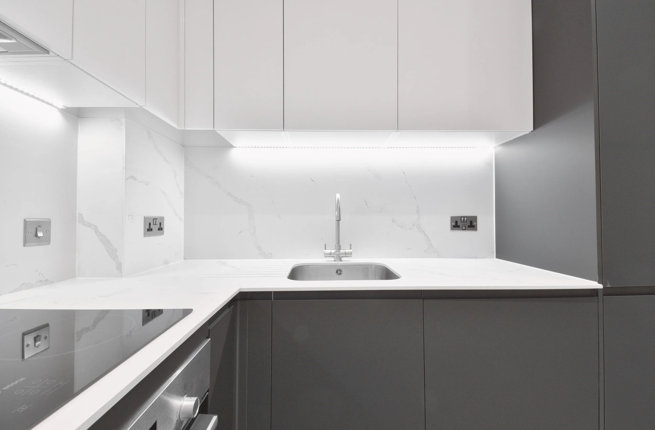 Modern kitchen with white marble backsplash, white countertop, gray cabinets, and built-in stovetop.