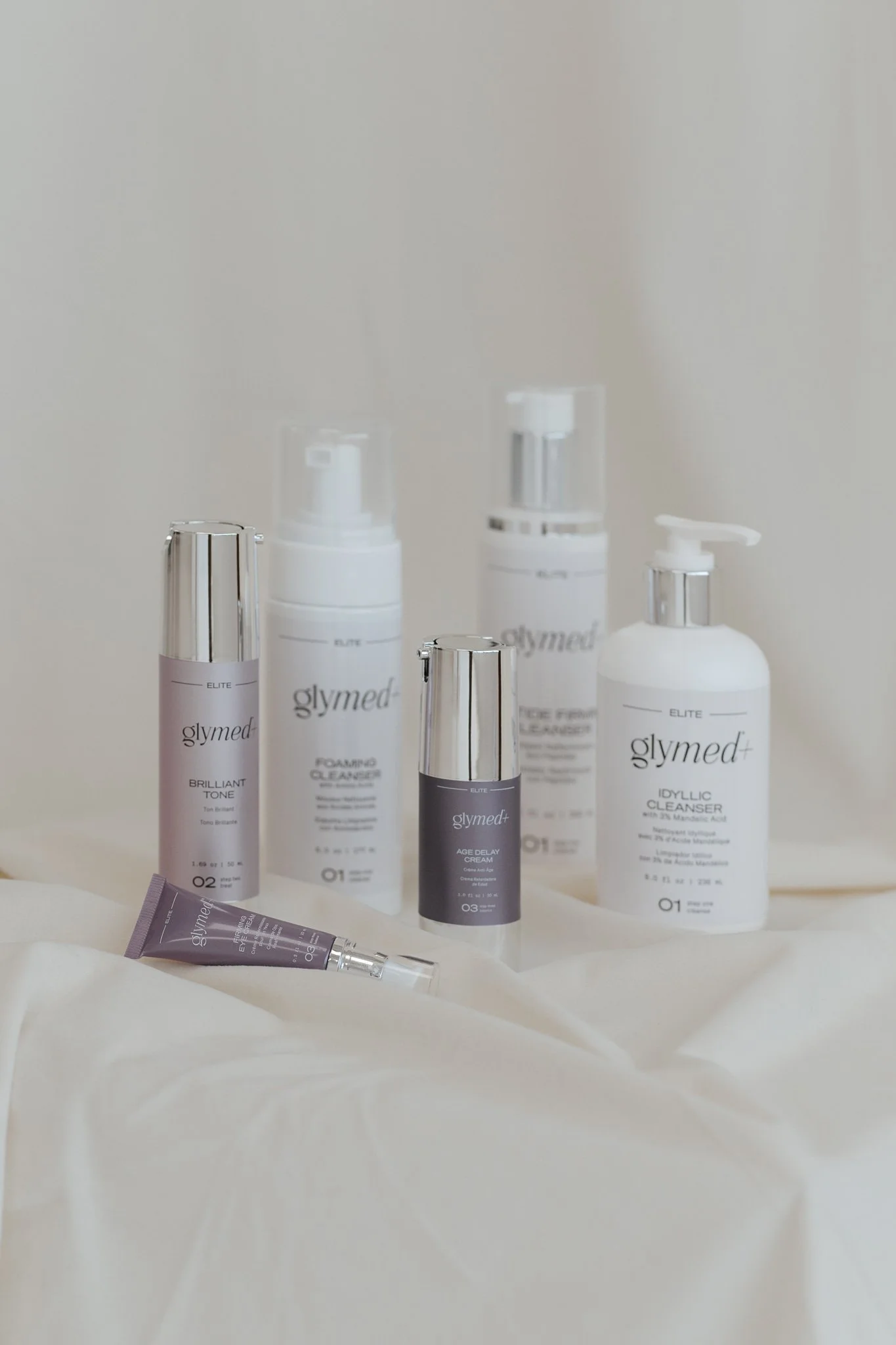 Various skincare products from the brand Glymed displayed on a white surface in front of a plain background, including bottles and tubes with labels.