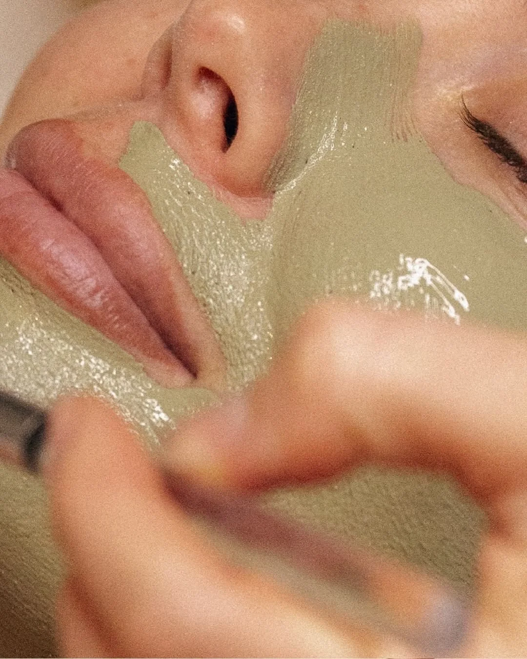 Close-up of a woman applying a gold facial mask, with her eyes closed.