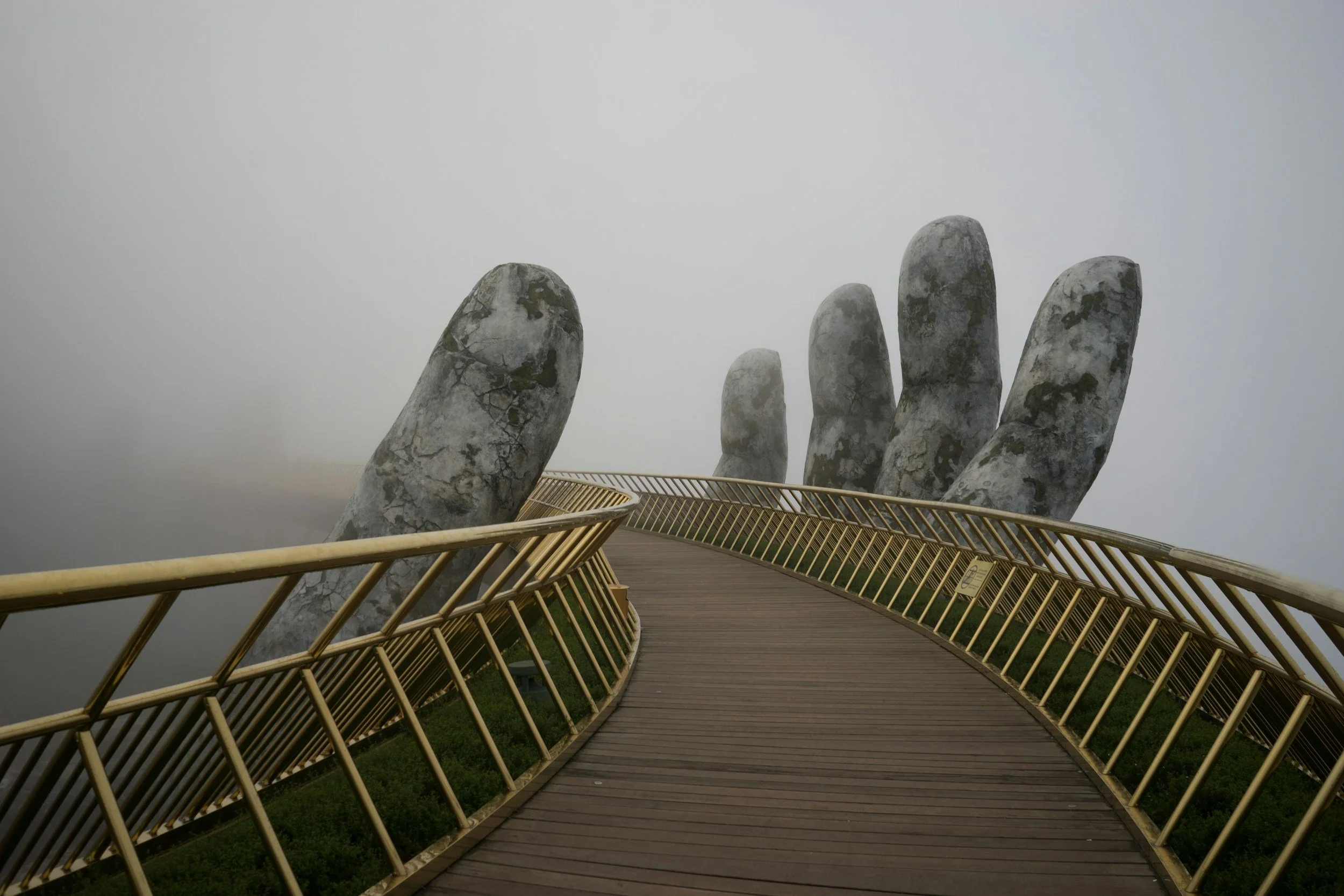 A pathway leading to a giant hand sculpture made of stone on a foggy day.