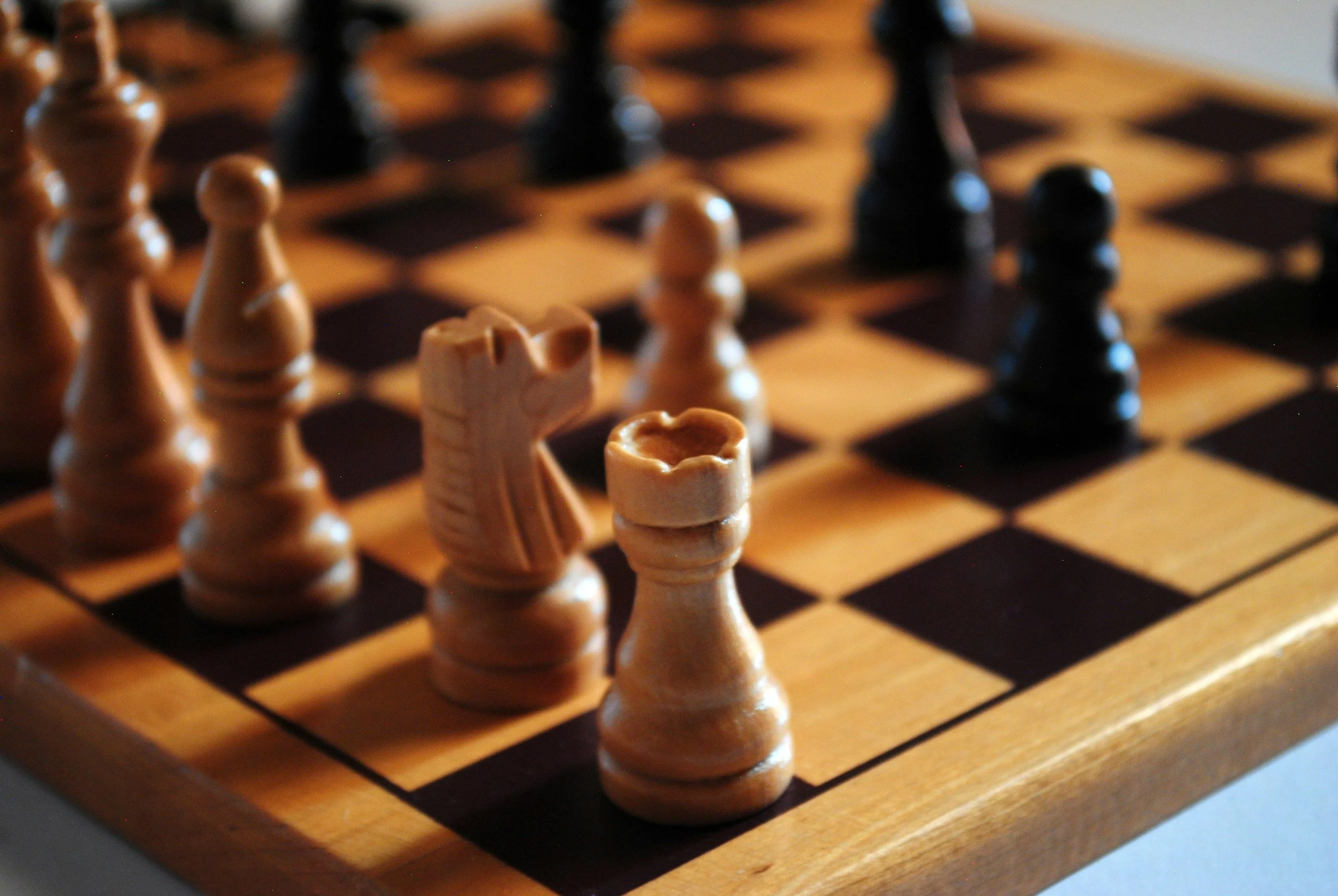 Close-up of a wooden chessboard with light and dark chess pieces set for a game.